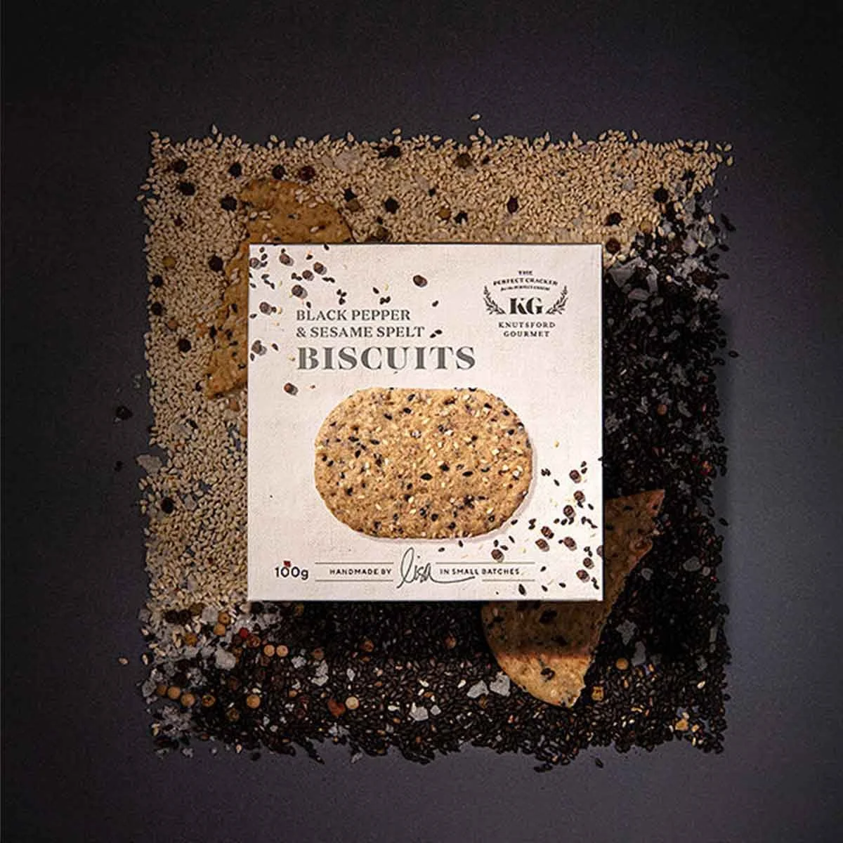 A stylished photograph of Knutsford Gourmet's Black Pepper and Sesame Spelt Biscuit packaging, positioned on top of the biscuits and black pepper and sesame spelt ingredients