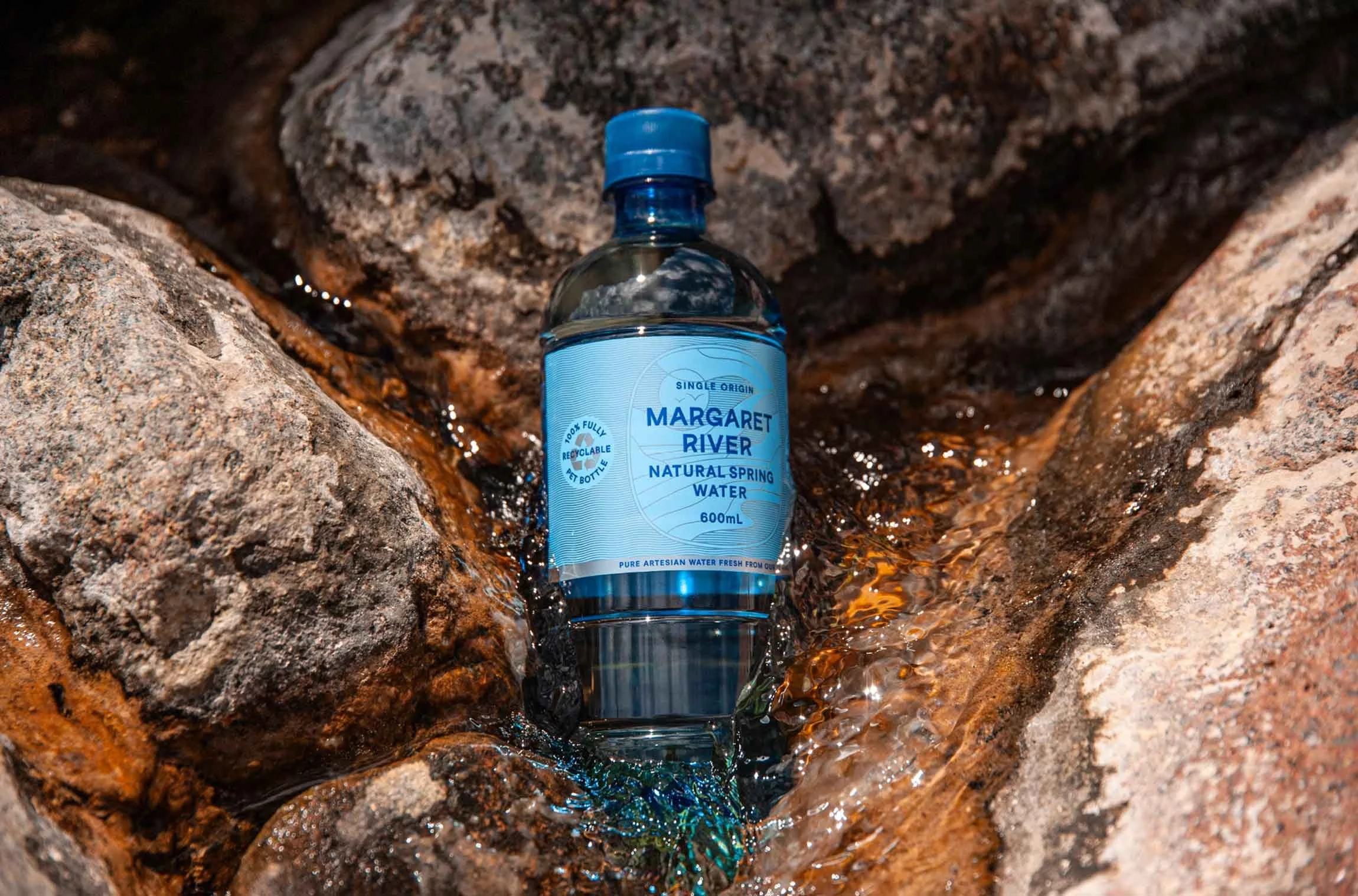 A 600ml bottle of Margaret River Natural Spring Water sitting in a creek bed with crystal clear water running past it