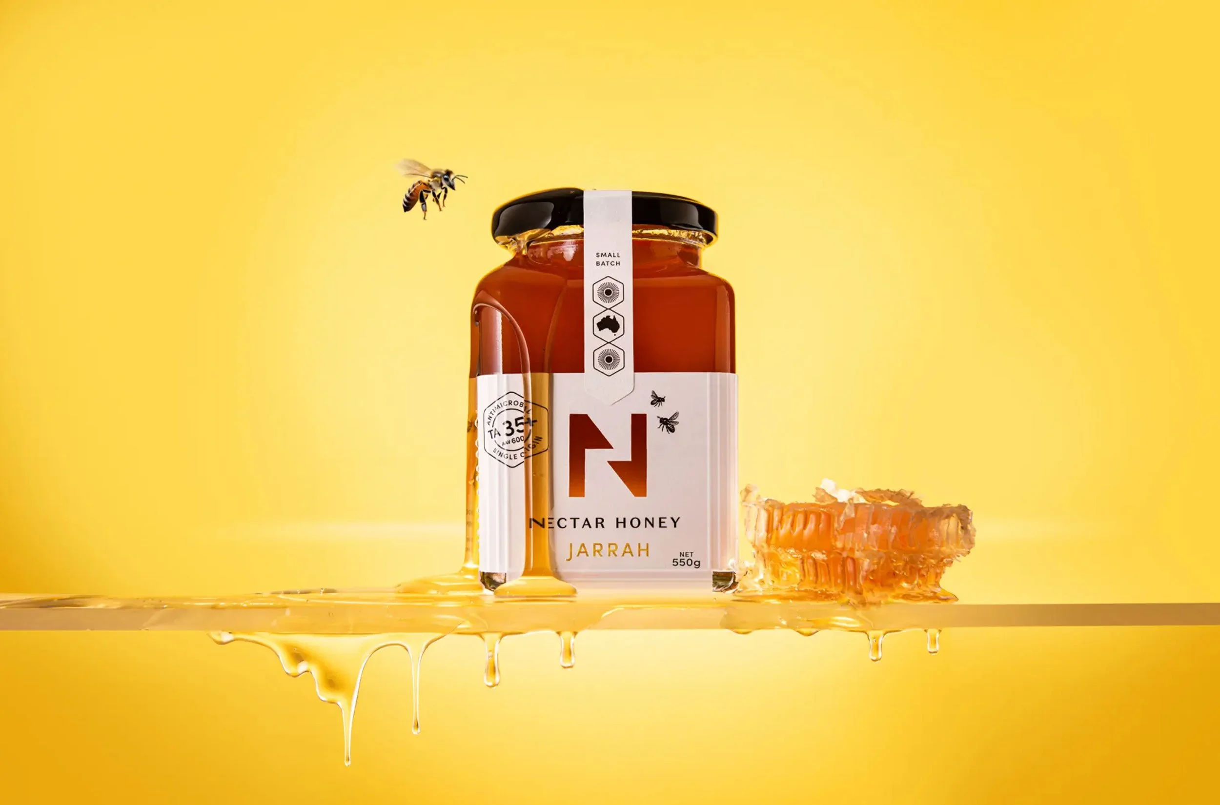 A stylised photograph of the label design of Nectar Honey's Jarrah honey with a bee buzzing around the jar and honey dripping down the side of the jar