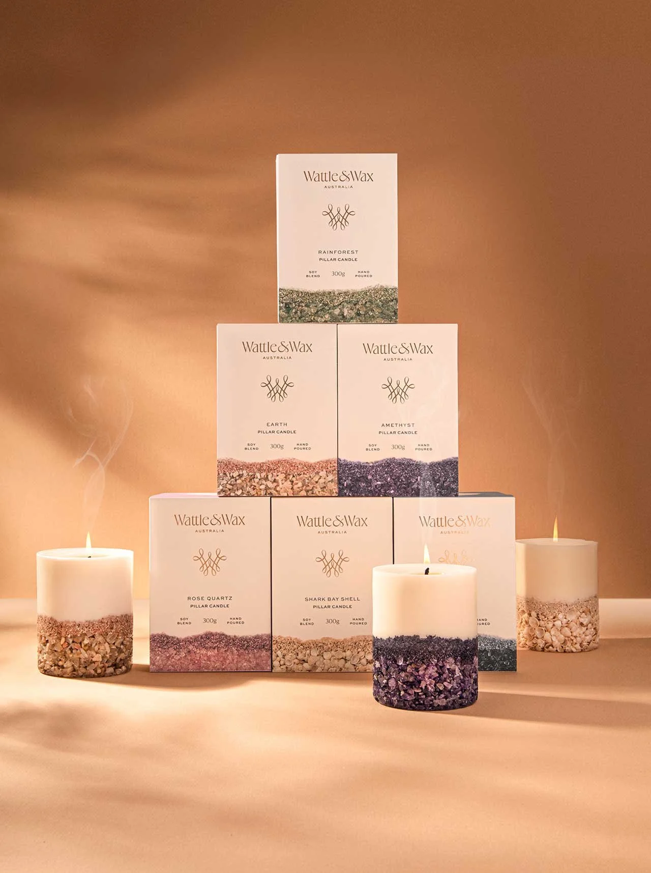 A stylised photograph of Wattle and Wax Australia's candle range, stacked into a pyramid with three of the candles from the range burning