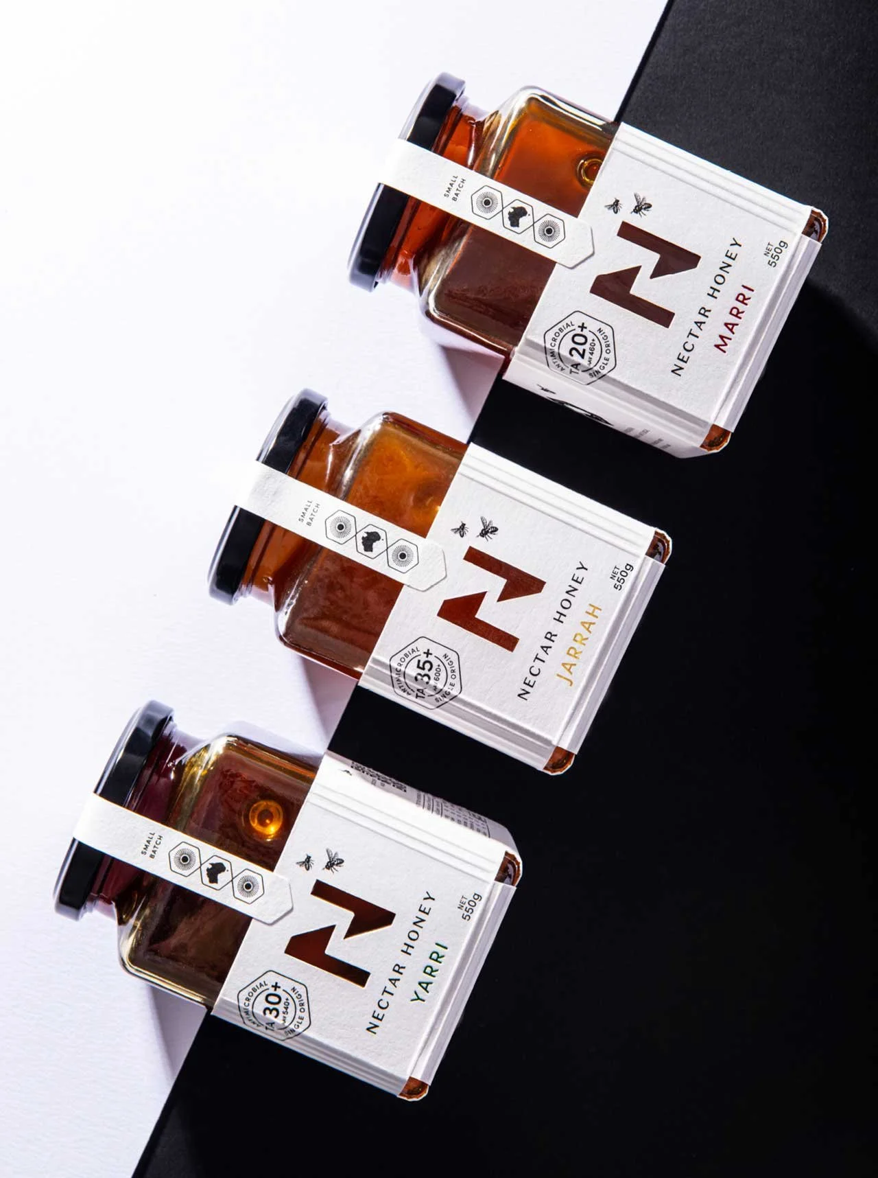 A stylised photograph of the label design of Nectar Honey's Jarrah, Marri and Yarri honey ranges, with the jars lying on a black and white background