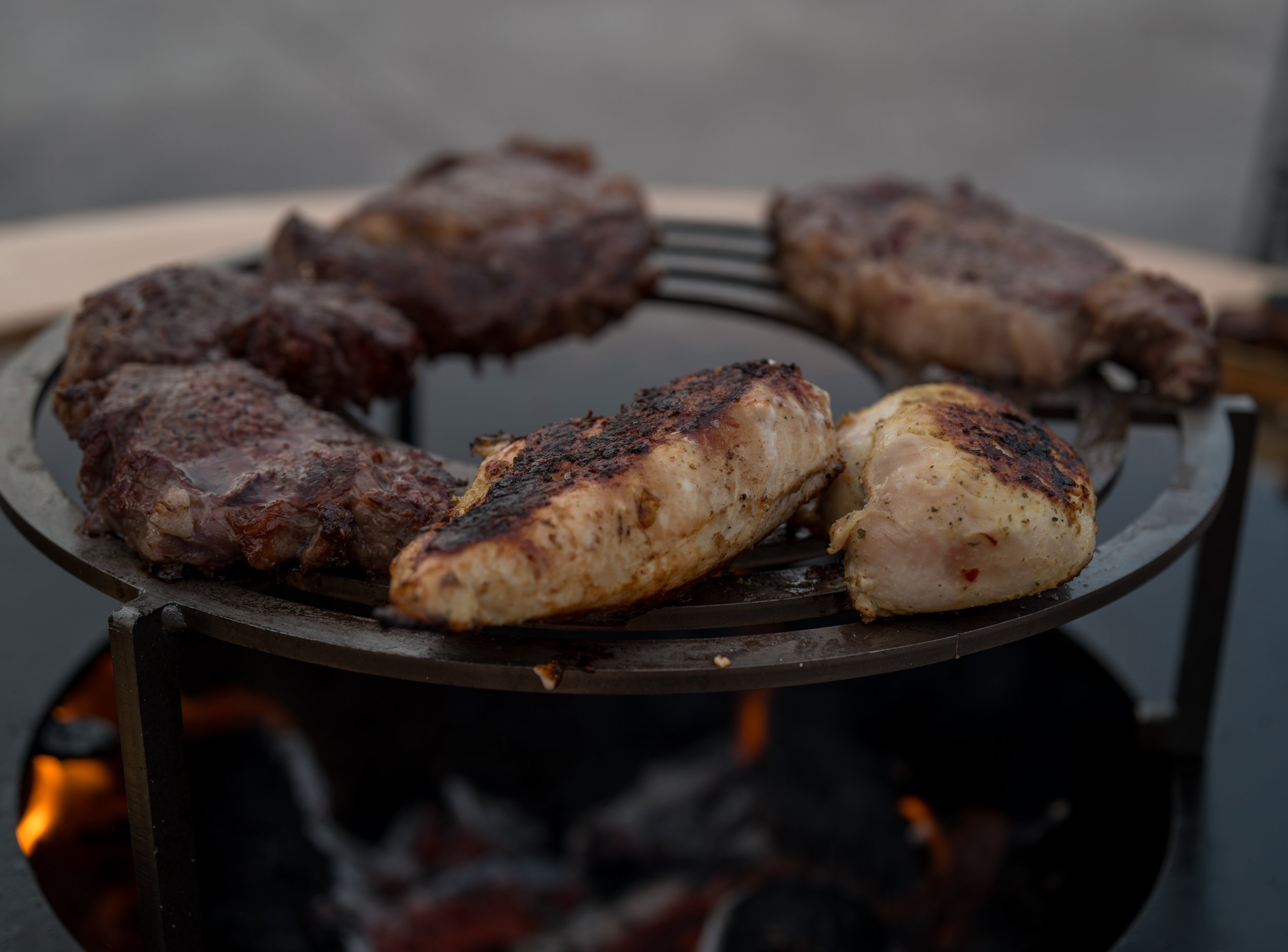 Grilled chicken and steaks on Sudfire fire pit grill with charcoal, live fire cooking and outdoor grilling