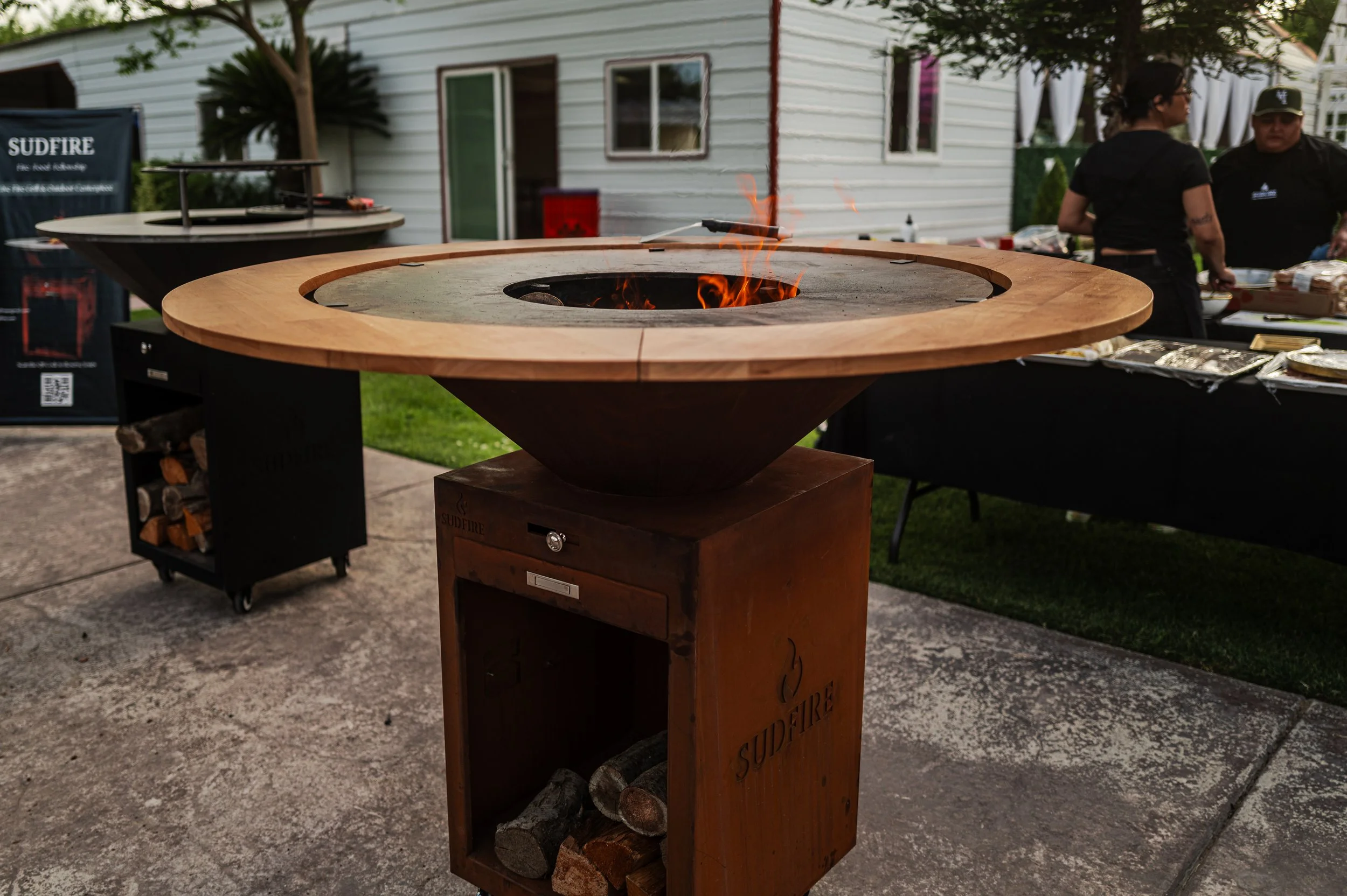 Sudfire fire pit grill table in backyard patio, outdoor cooking with friends and live fire gathering setup