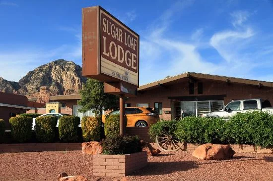 Sign for Sugar Loaf Lodge in a mountainous area with vehicles parked in front, surrounded by bushes and rocks.