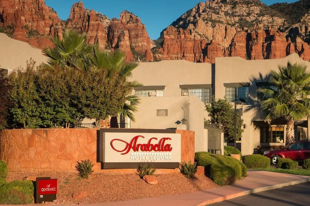 Exterior view of the Amabella Collection Hotel Sedona with red rock formations in the background, featuring palm trees and landscaping.