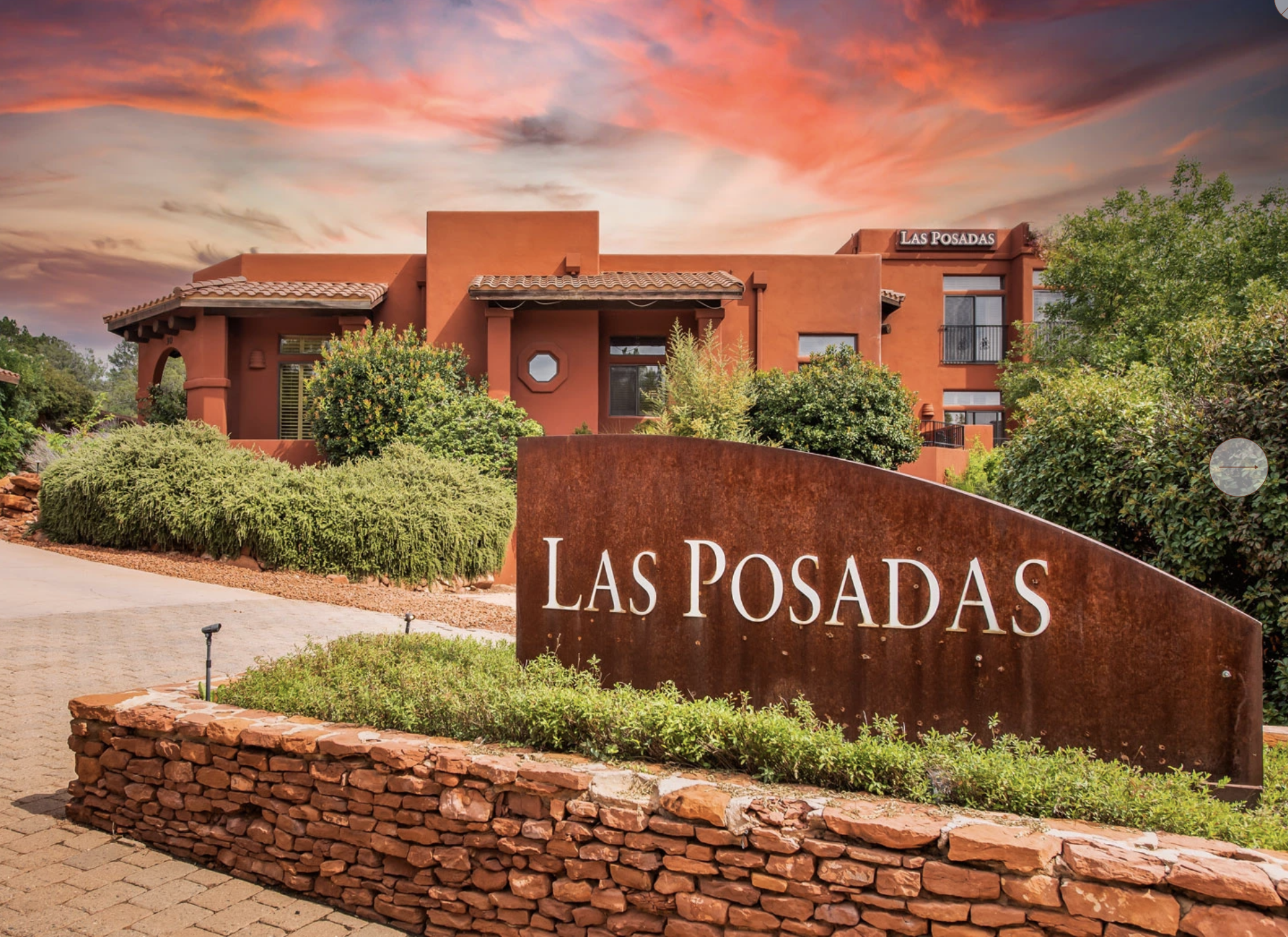 Residential building with a sign that reads 'Las Posadas' Hotel in front, set against a colorful sunset sky with greenery around.
