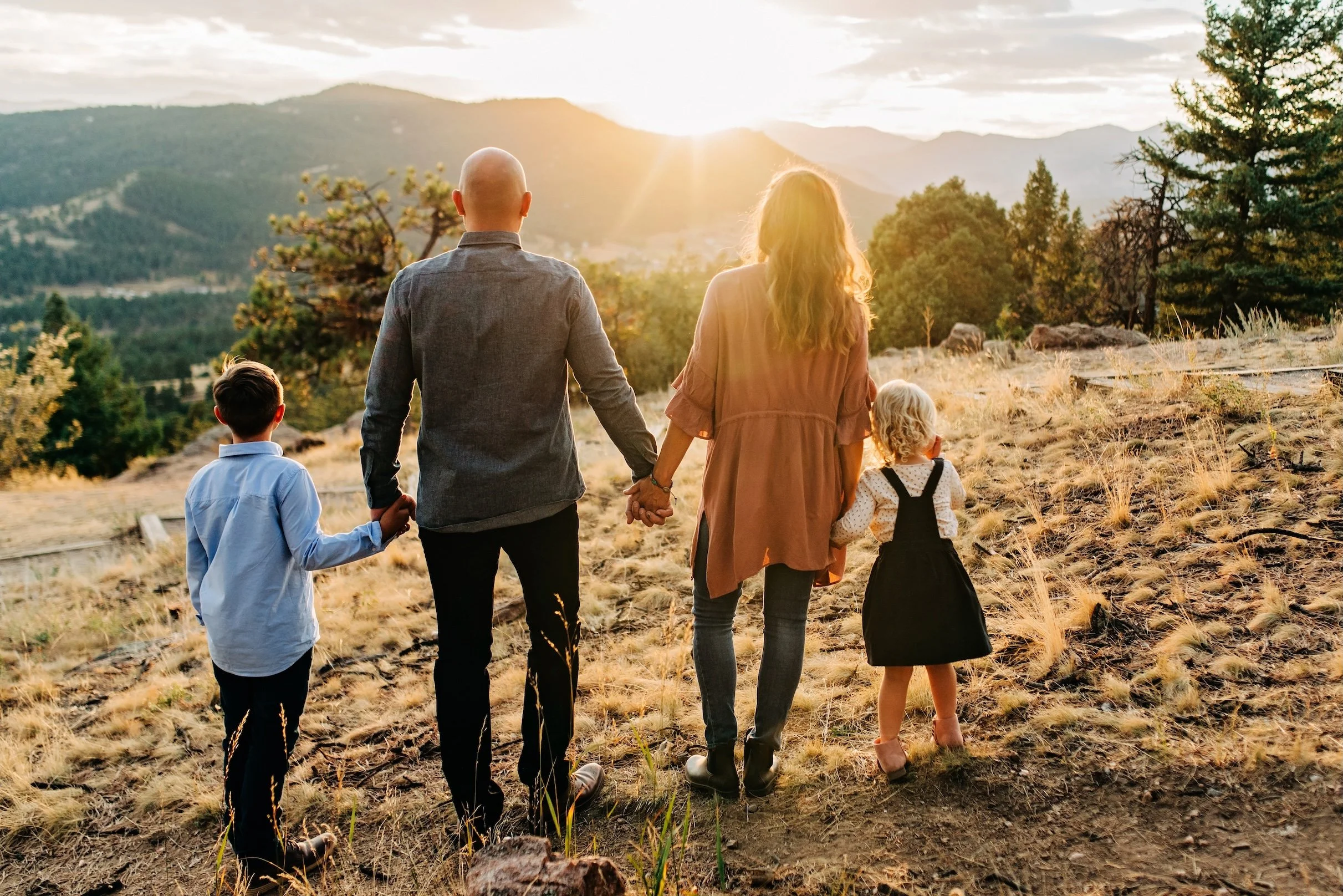 A family of four walking hand in hand on a trail in a scenic mountain landscape during sunset.