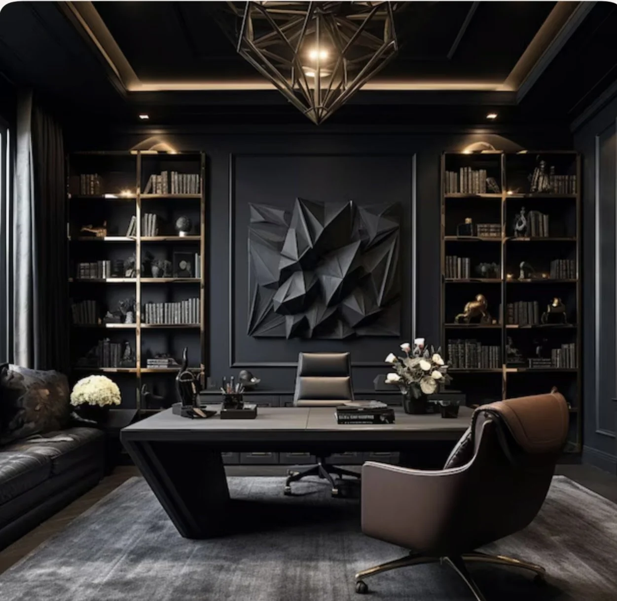 A modern, dark-themed office with a large wooden desk, black leather chair, beige armchair, and two tall black bookshelves filled with books and decorative objects. A geometric black wall art piece decorates the wall behind the desk, and a stylish pendant light hangs from the ceiling. The room is decorated with flowers, and a grey rug covers the floor.