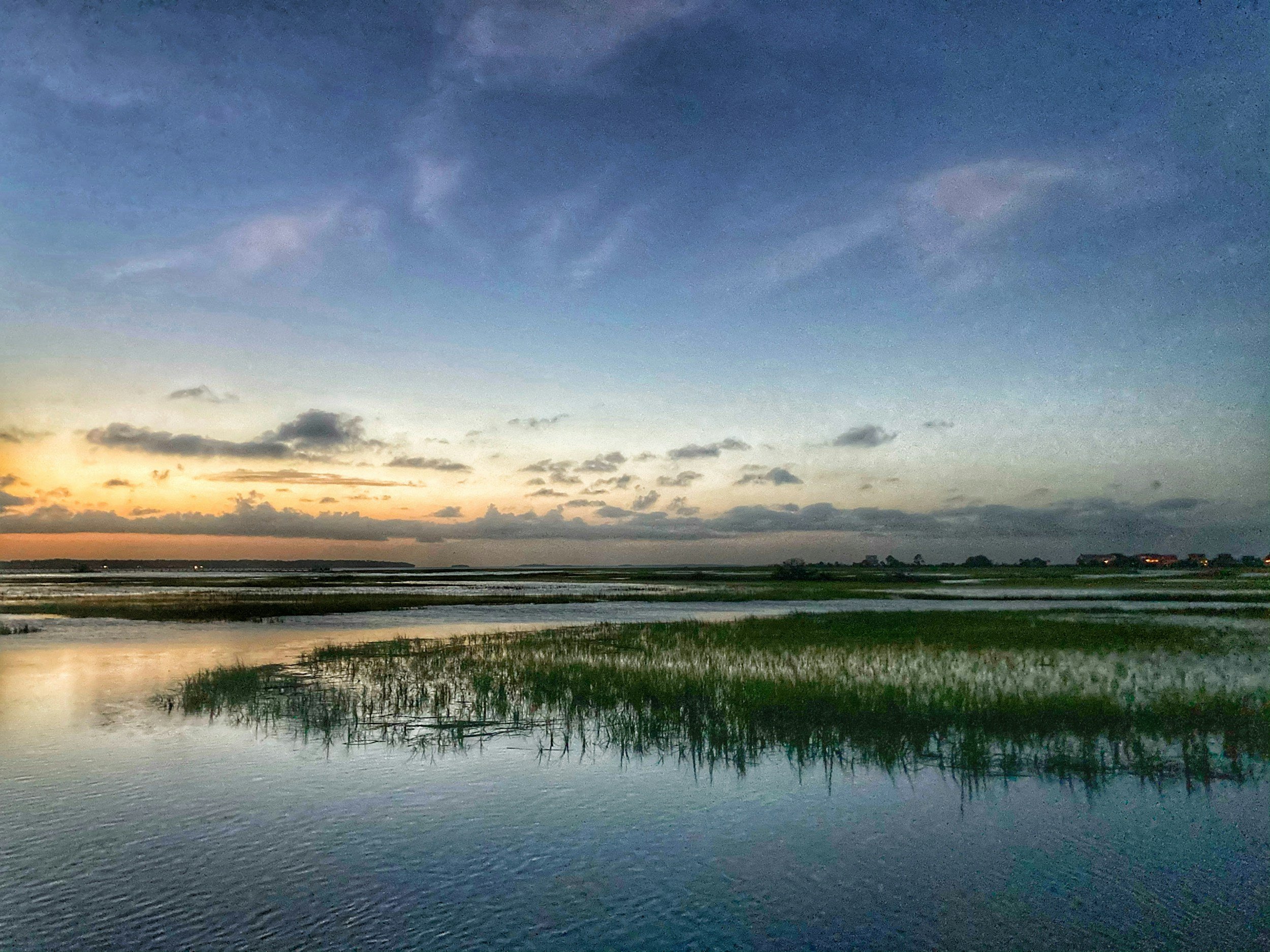 Scenic view of a river or wetland at sunset with a colorful sky and clouds in the background.