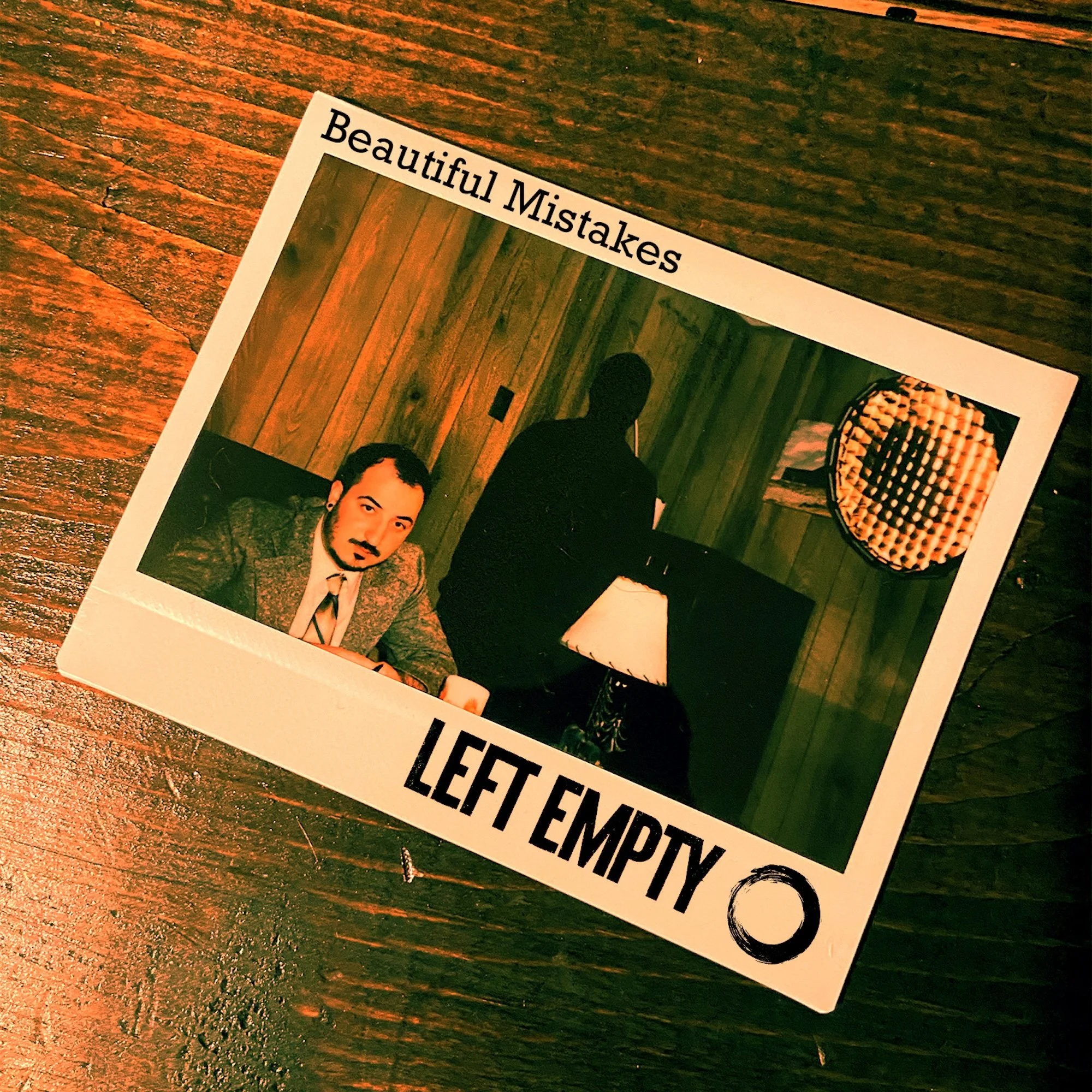 A printed photo with the words "Beautiful Mistakes" at the top, showing part of a woman with a tattoo and a man in a suit on a wooden floor.
