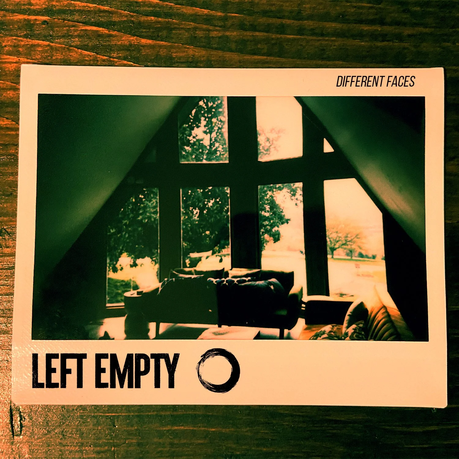 A photograph of a living room with large windows showing trees and sunset outside. The room has a dark sofa, a chair, and some indoor plants. The photo is part of a card labeled "Different Faces" with the text "Left Empty" and a circle below it.