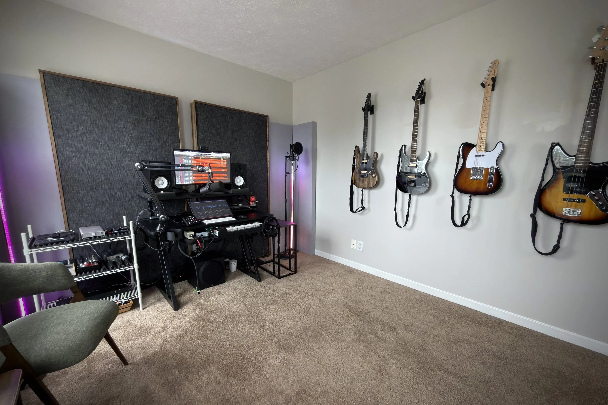 Music studio with four electric guitars hanging on the wall, a computer with music production software, studio monitors, and various audio equipment.