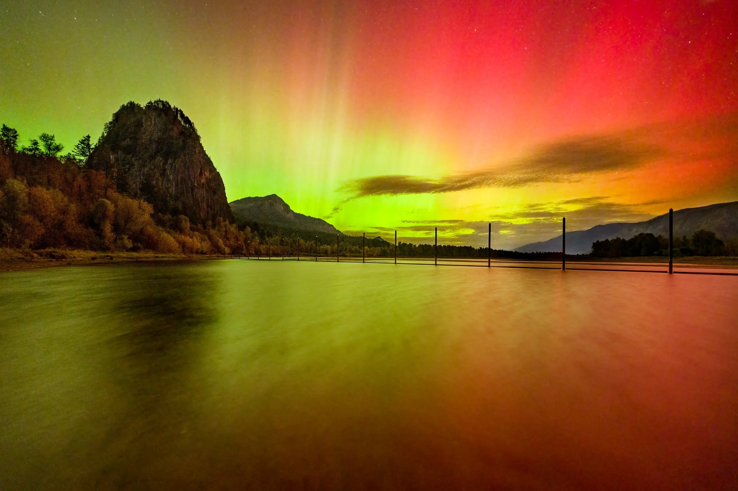 Aurora borealis over a lake with mountain and trees in the background at night.