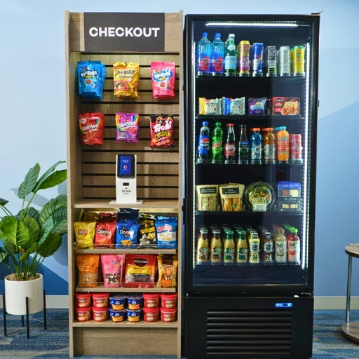 Snack vending machine and refrigerated drink cooler against a blue wall, with a potted plant nearby.