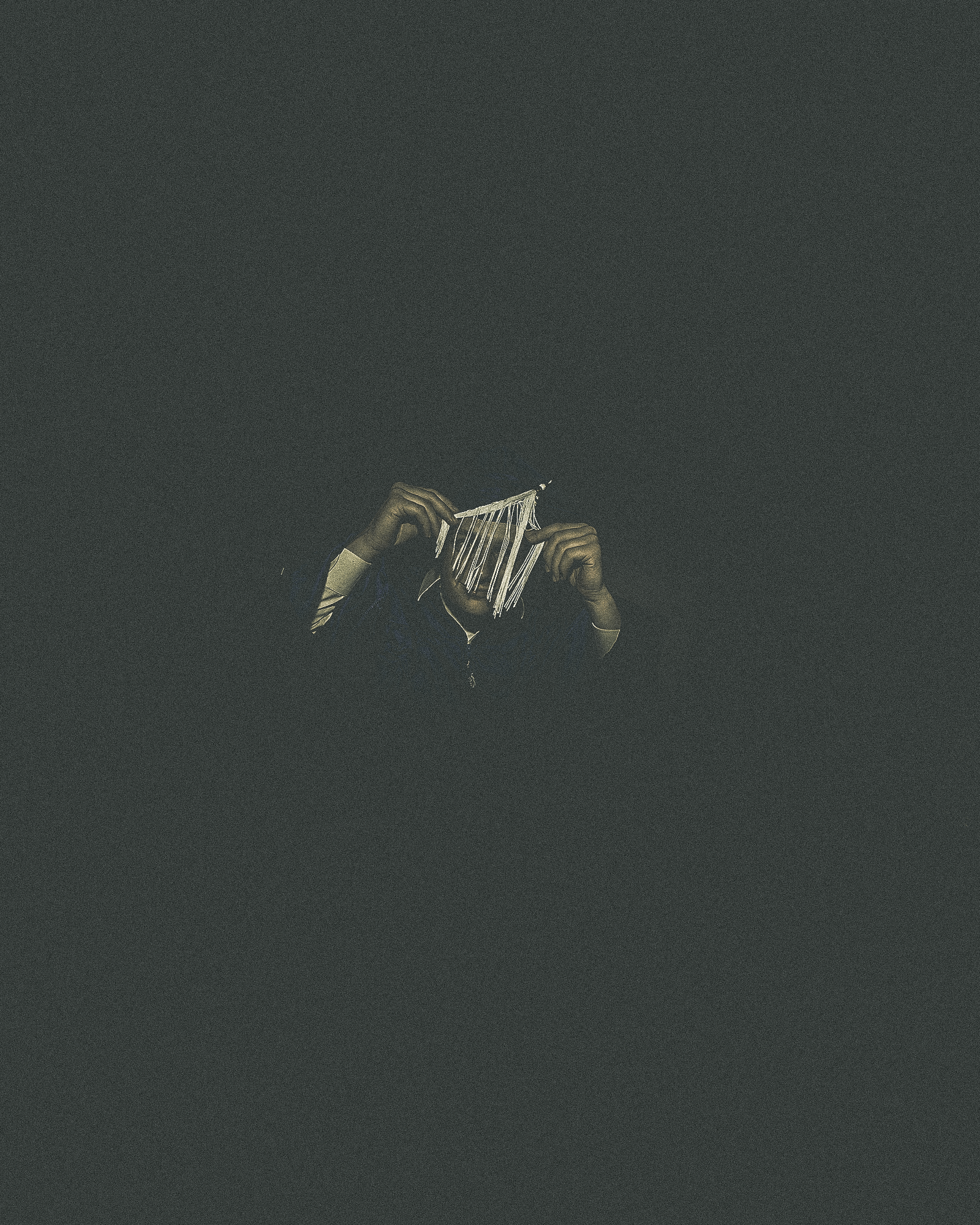 Person holding handmade paper or string craft against dark background.