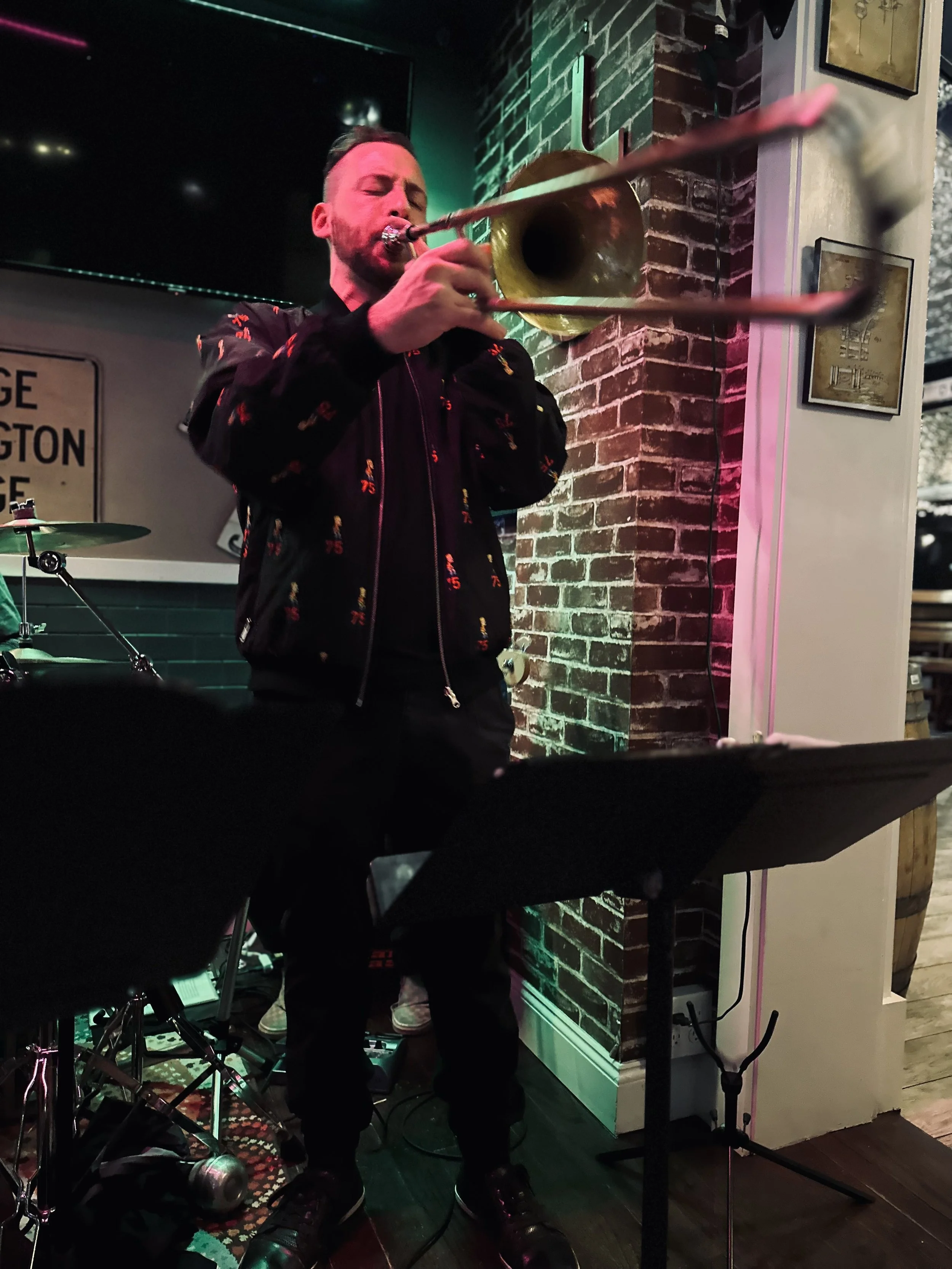 A man playing the trumpet in a dimly lit room with brick walls and music equipment.