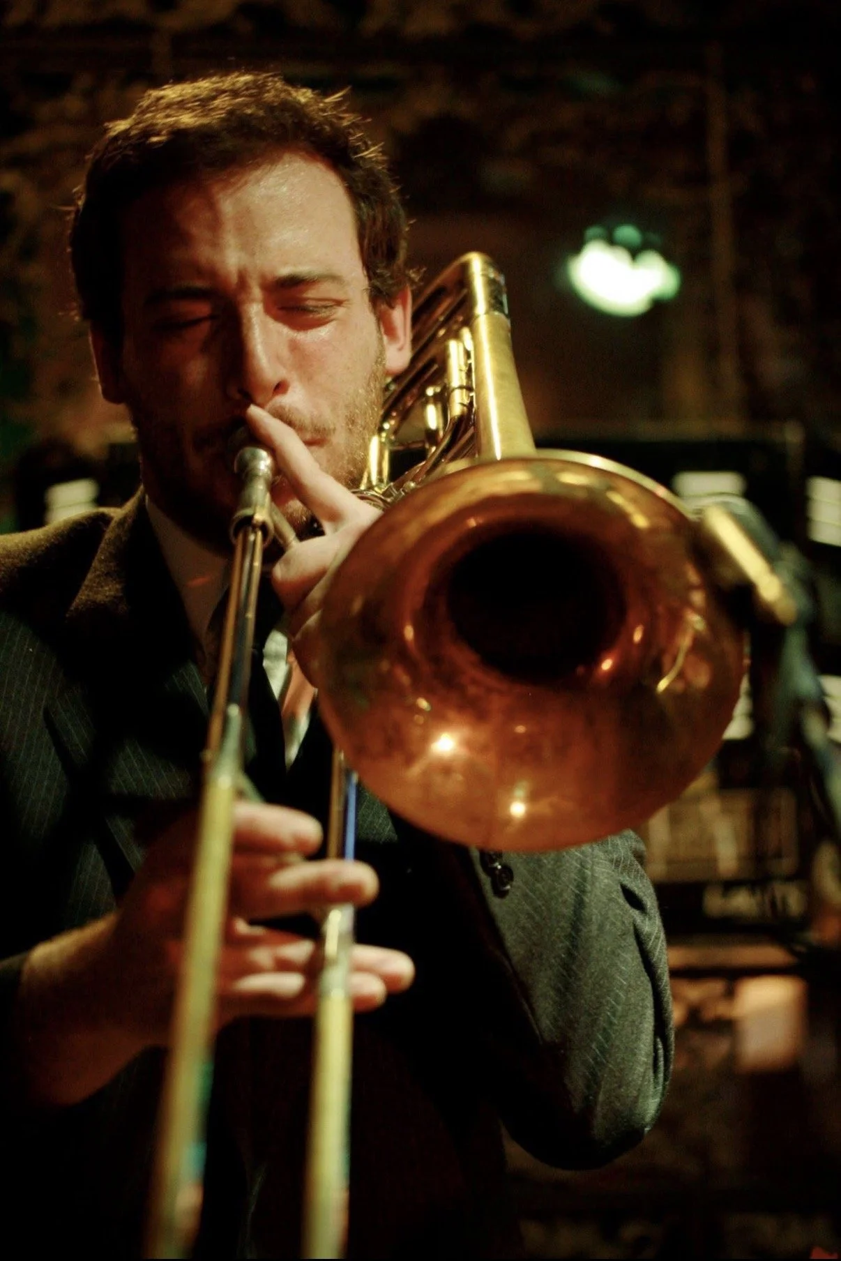 A man playing a trumpet, with his eyes closed, in a dimly lit environment.