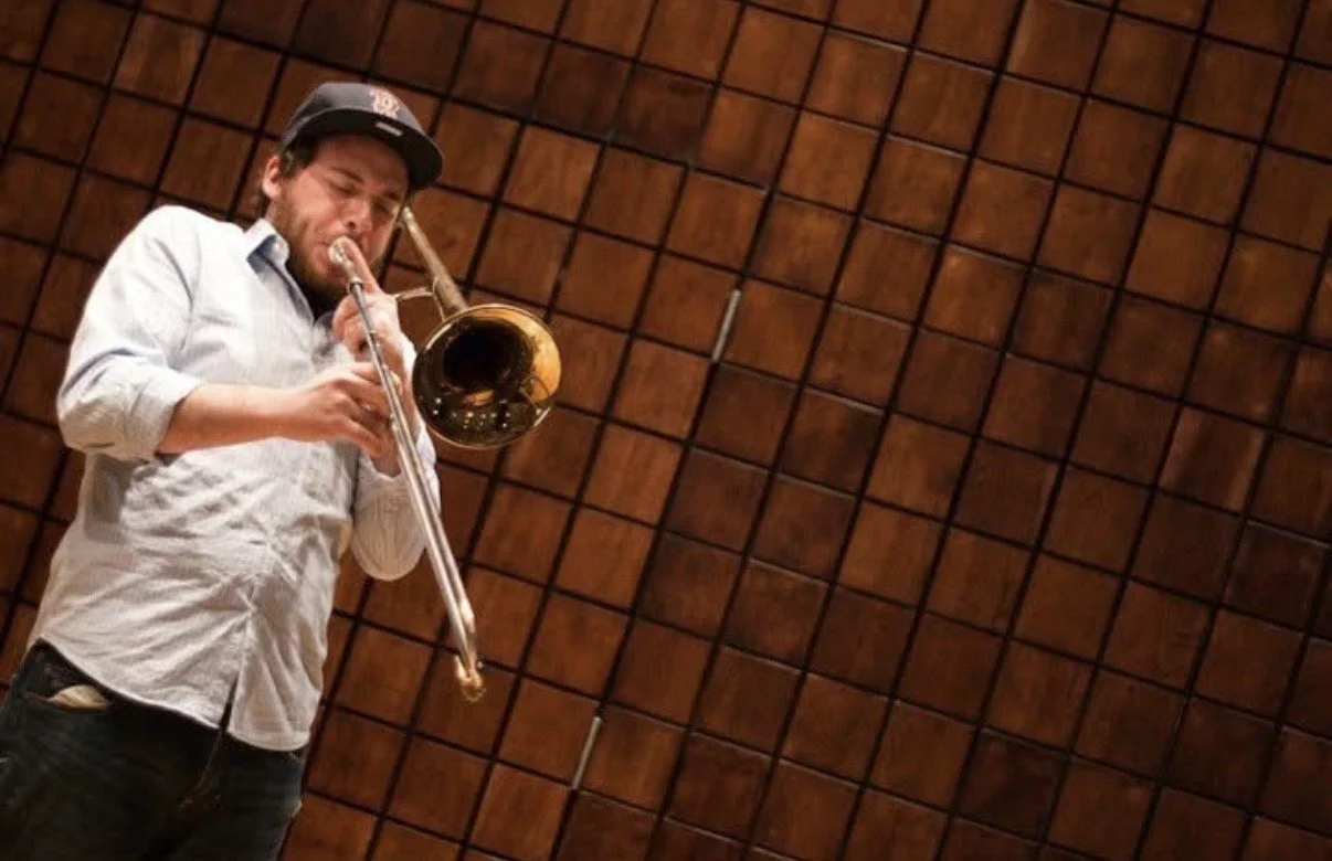 A man playing a trumpet in a room with wood-paneled walls.