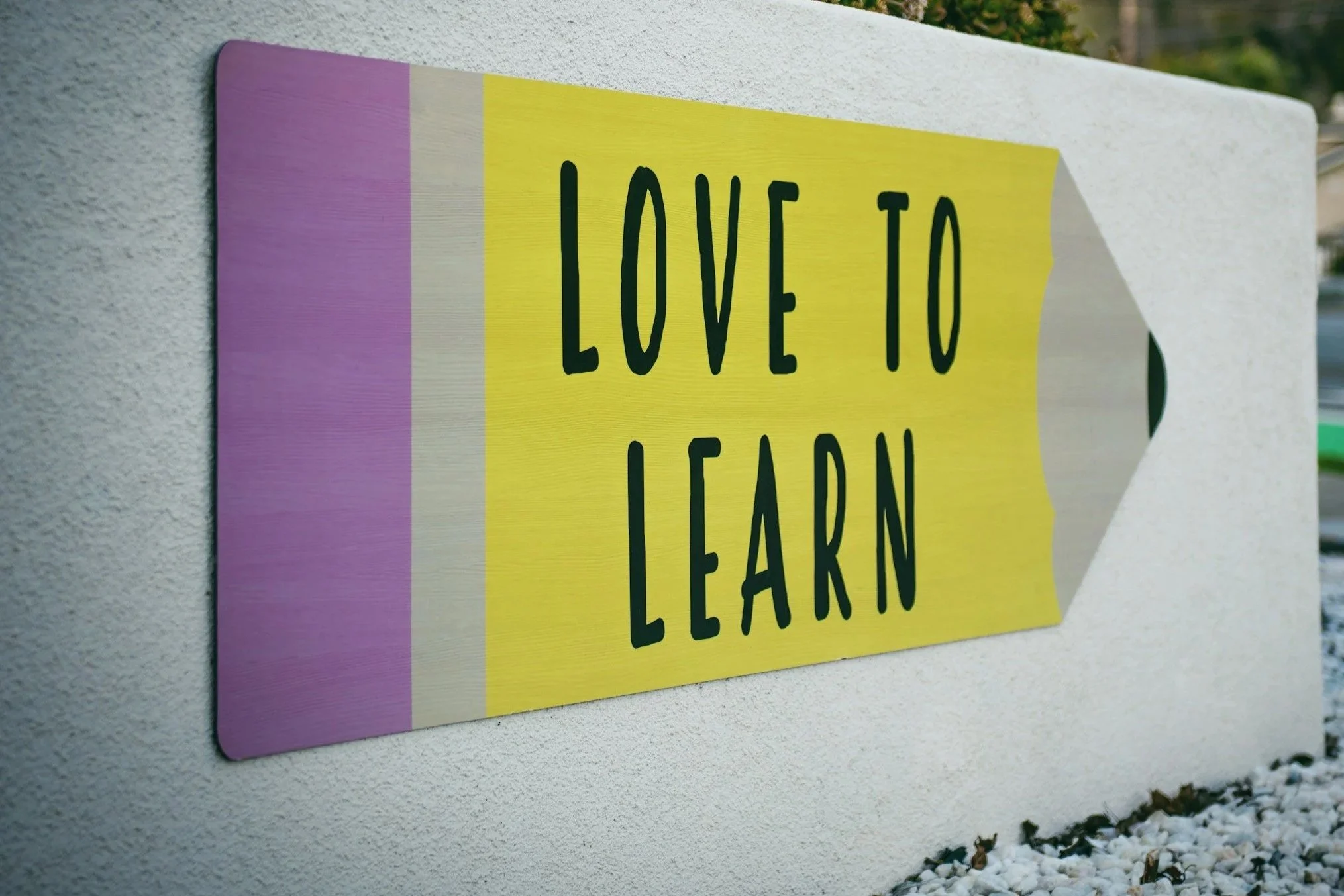 Yellow and purple sign with black text saying 'Love to Learn' attached to a white wall outdoors.
