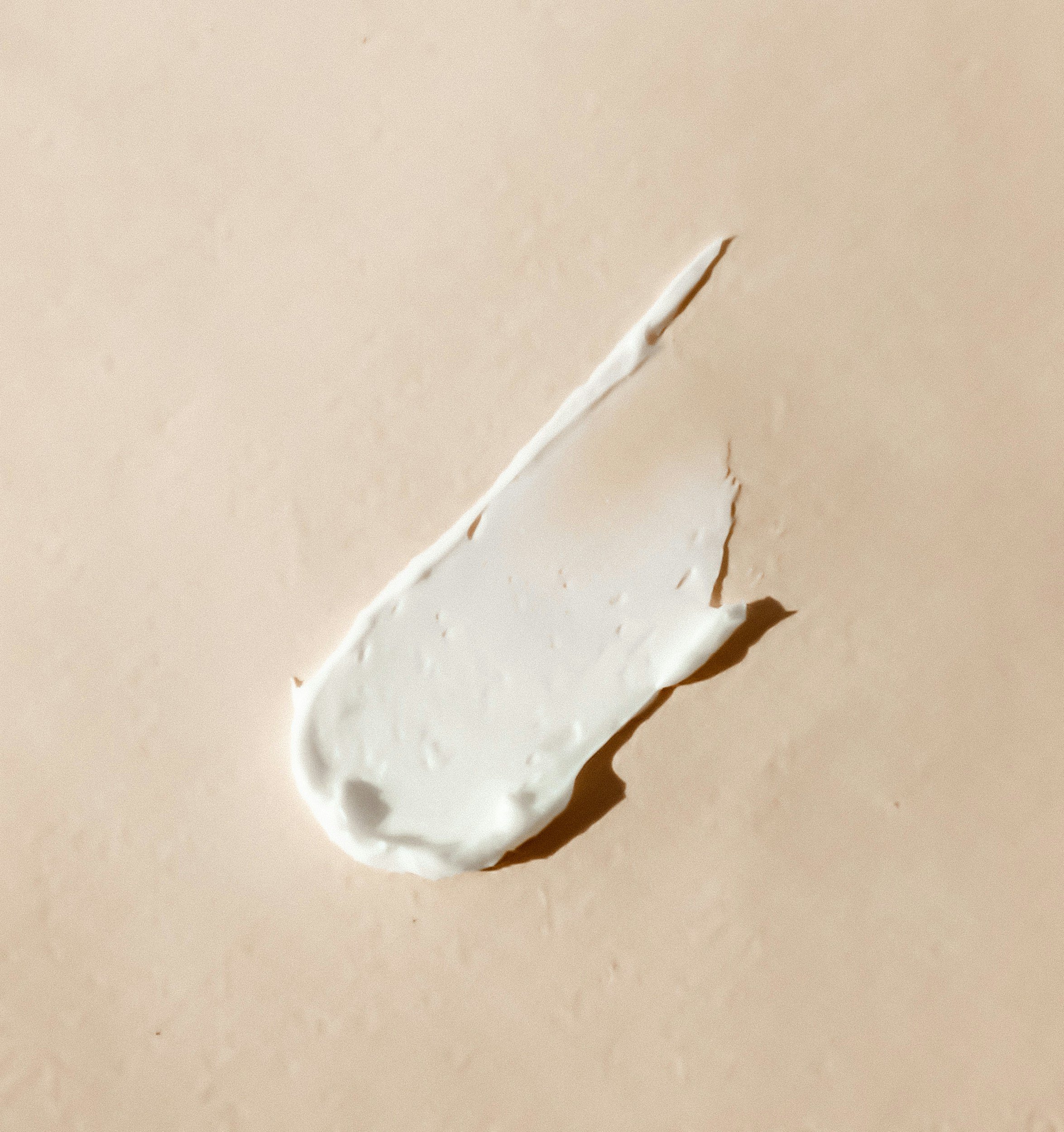 A smear of white cream or lotion on a beige surface.