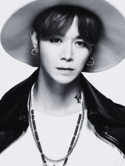 Une personne portant un chapeau large, des boucles d'oreilles, un t-shirt blanc et une veste en cuir, avec des chaînes autour du cou, en noir et blanc.