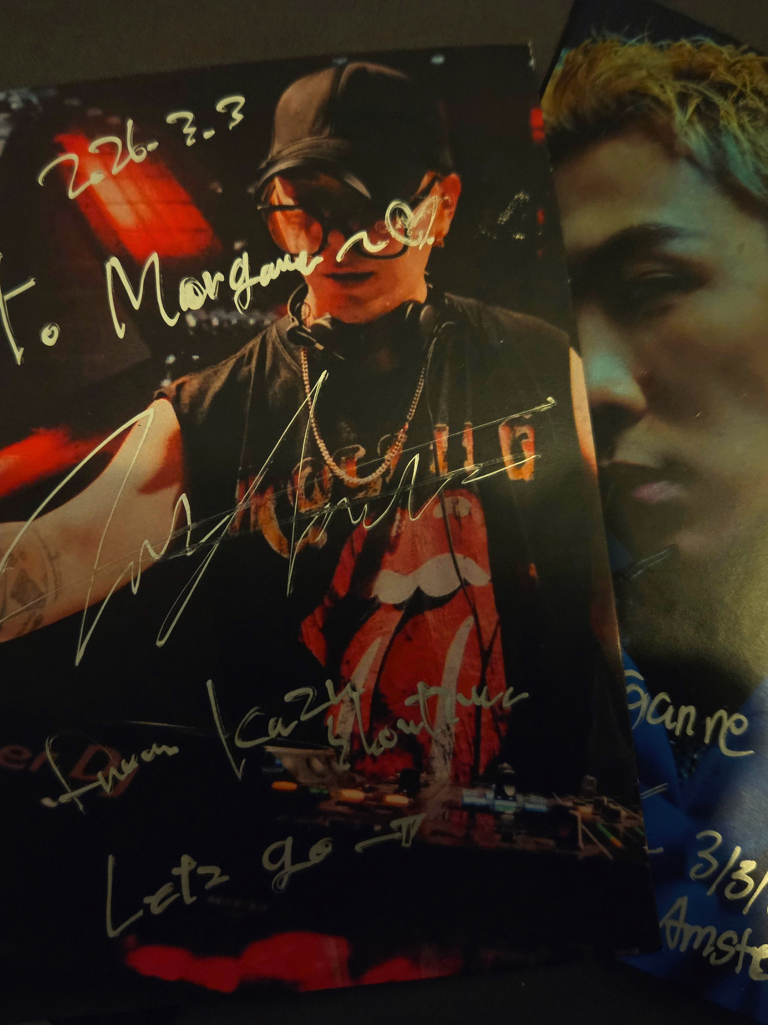 Photo d'une personne portant des lunettes de soleil, un collier, avec des signatures en French et des inscriptions en couleur, probablement dans un contexte musical ou artistique.