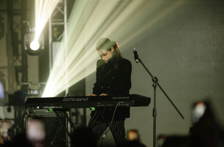 Une femme joue du clavier Roland lors d'une performance sur scène avec des lumières en arrière-plan.