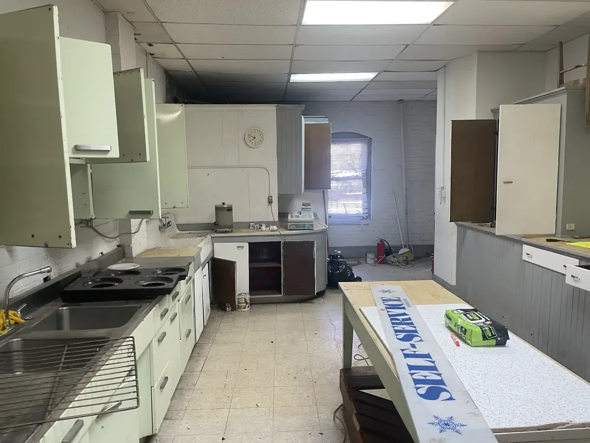 An empty, cluttered kitchen with disorganized cabinets, a table with a SERVPRO sign, and cleaning supplies on the counter.
