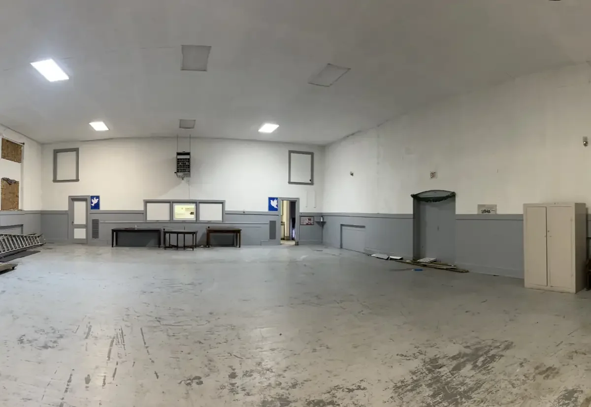 Empty, unfinished room with gray walls, a few tables, ladders, and a cabinet, no furnishings or decorations.
