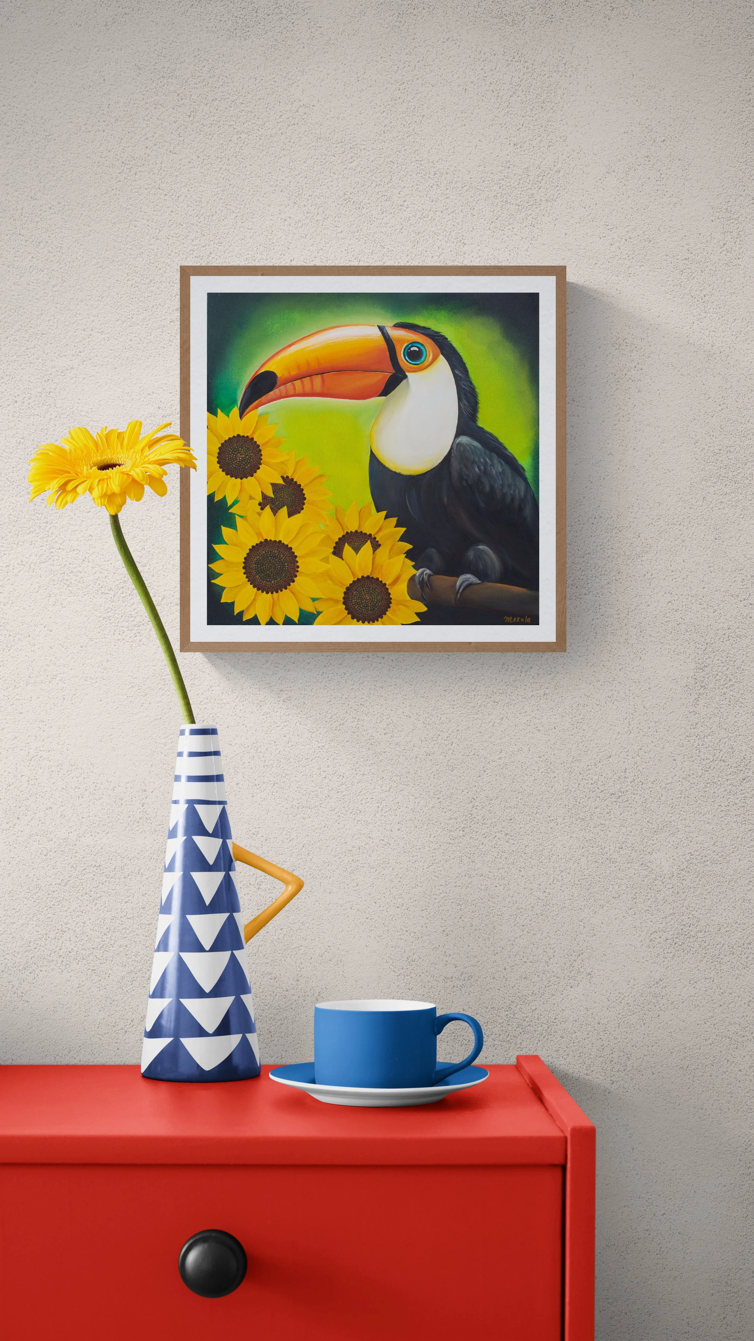 A colorful still life scene with a blue mug on a saucer, a tall decorative vase with a sunflower, and a framed painting of a toucan bird surrounded by sunflowers on a beige wall.