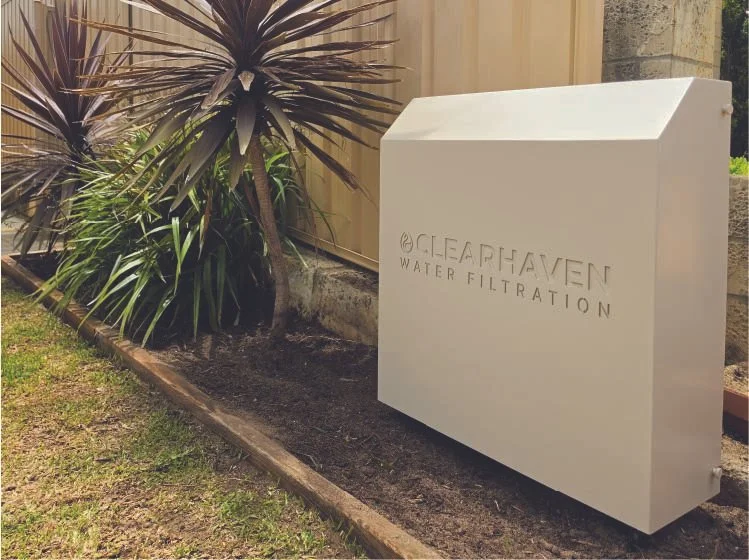 ClearHaven TripleShield whole-home water filtration system with a Paperbark powder-coated cover, professionally installed beside a garden in Hocking, Perth.