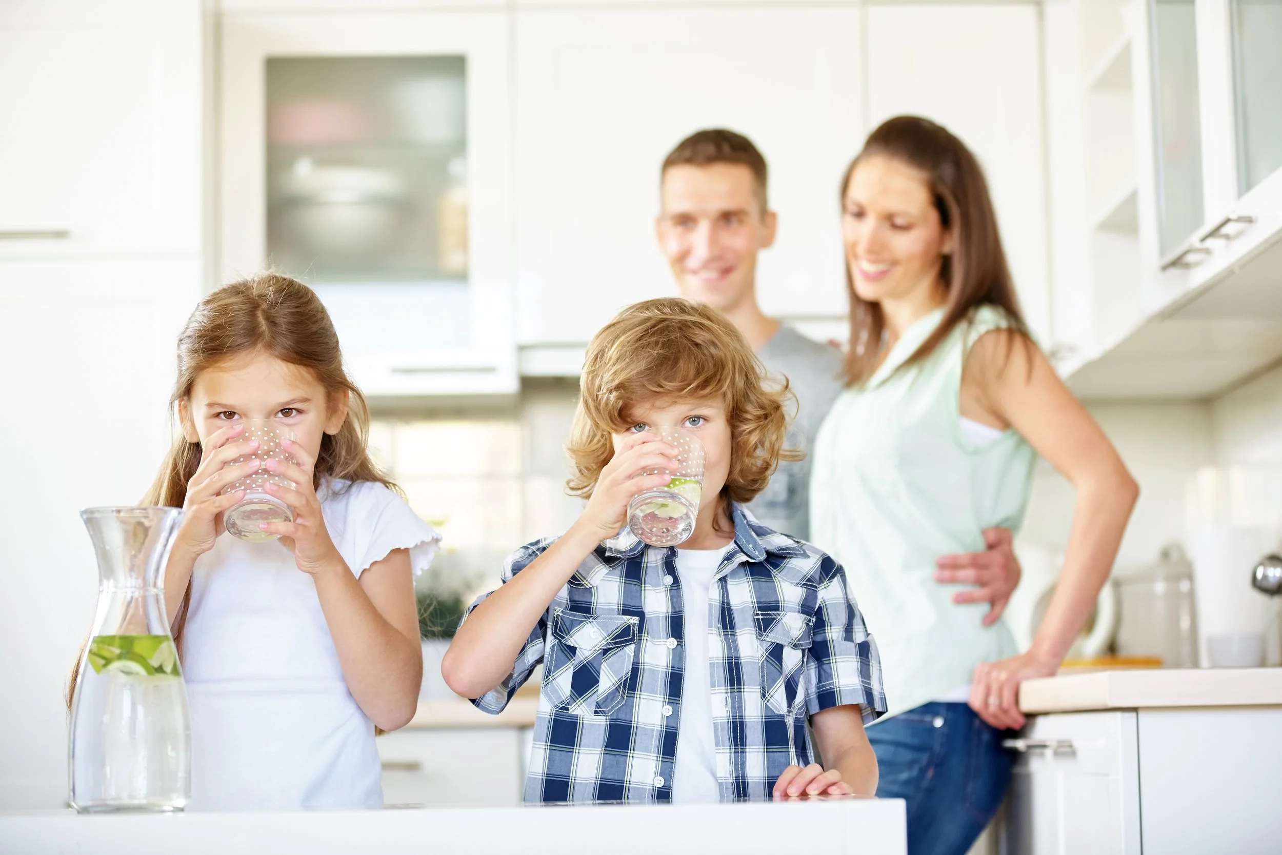 Children drinking clean, filtered water at home while their parents look on, illustrating how a ClearHaven whole-home water filtration system provides healthier drinking water for families in Perth.