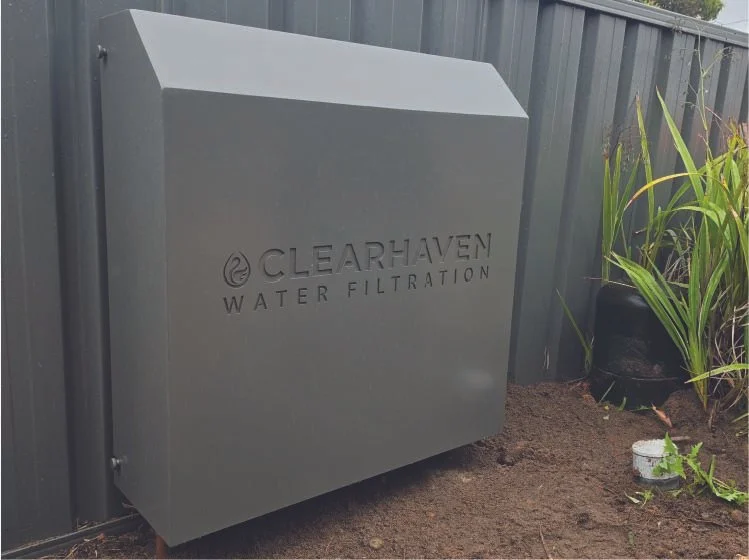 ClearHaven TripleShield whole-home water filtration system with a Woodland Grey powder-coated cover, professionally installed against a matching Colorbond fence in Carlisle, Perth.