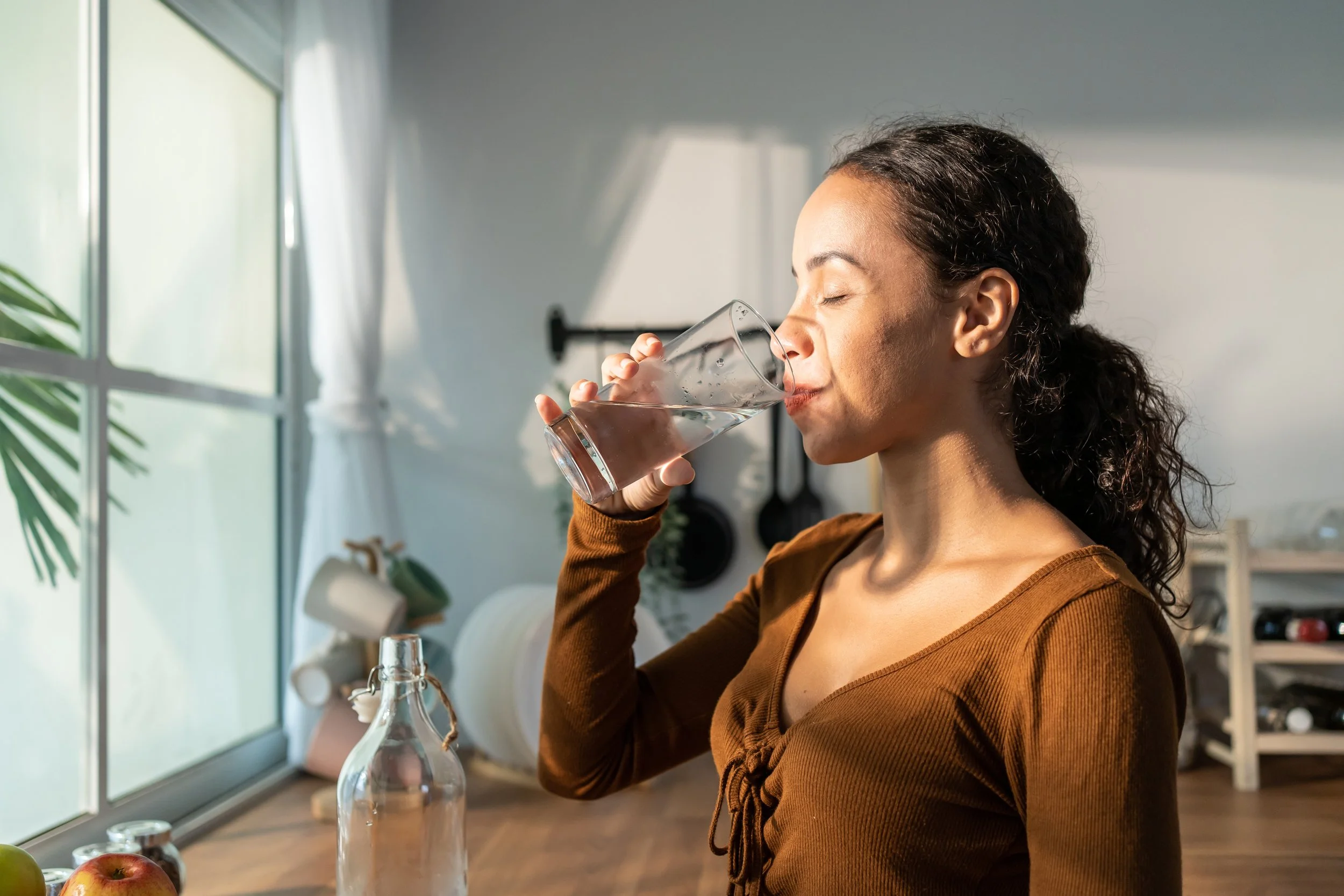 Woman enjoying a glass of clean, filtered water in a Perth home, highlighting the hydration benefits of ClearHaven whole-home water filtration.