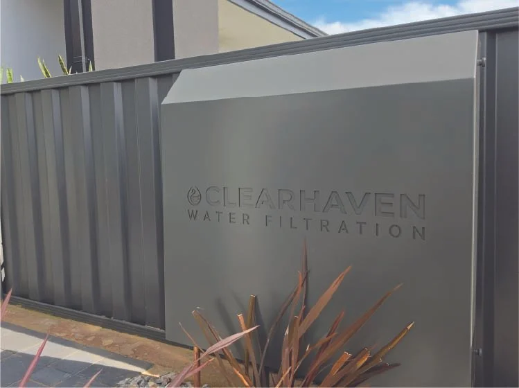 ClearHaven TripleShield whole-home water filtration system with a Woodland Grey powder-coated cover, professionally installed against a matching Colorbond fence in Perth, featuring a sleek, beautifully integrated design.