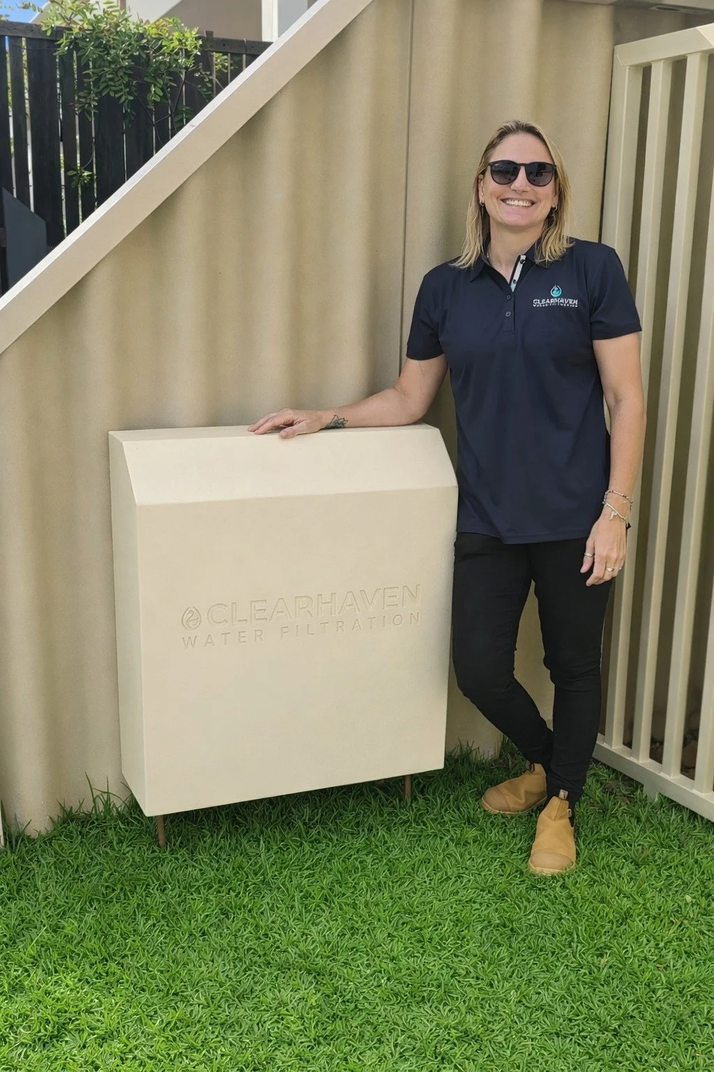Jade De Joode, founder of ClearHaven Water Filtration, standing beside a premium whole-home water filtration system with a custom powder-coated cover at a Perth home.