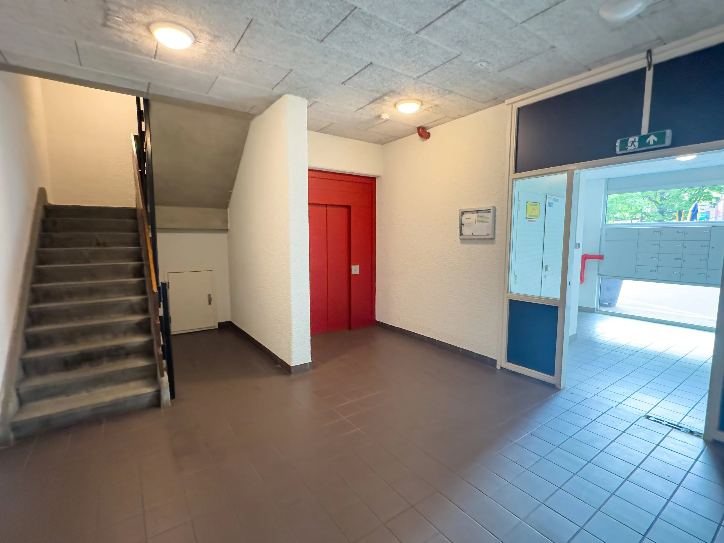 Inside building lobby with stairs, elevator with red doors, and mailboxes in the background.