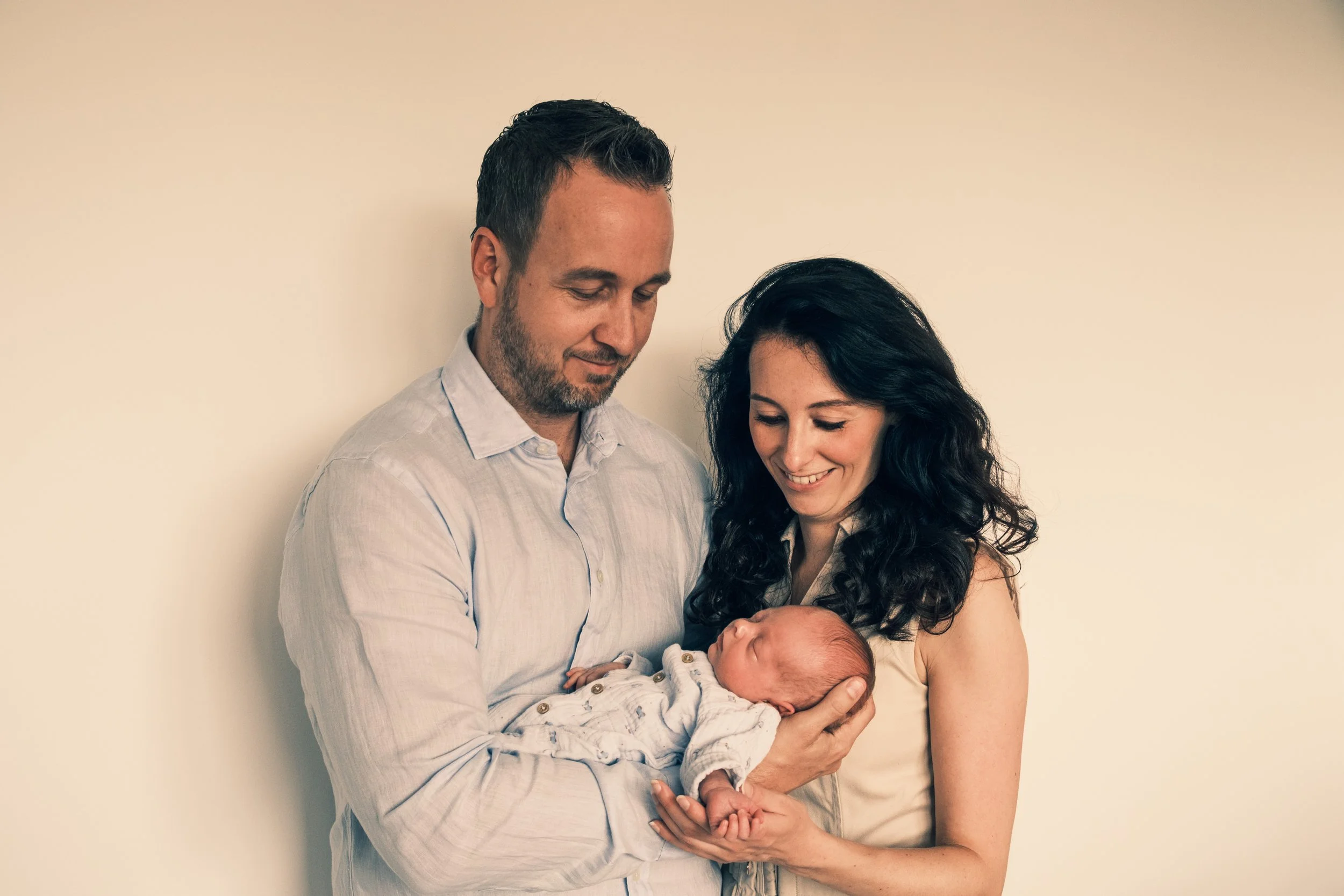 A couple holding a newborn baby and smiling at the baby.