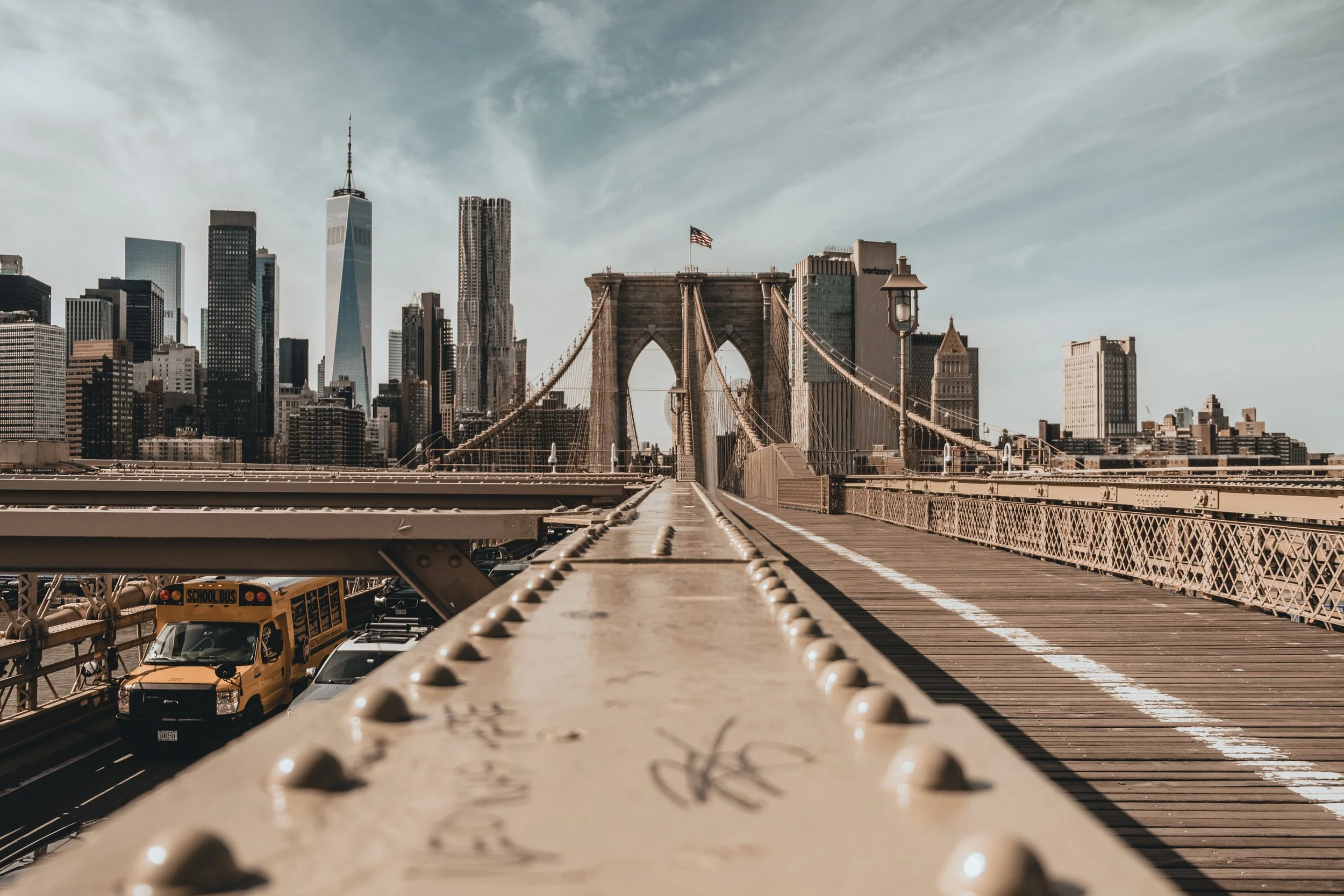 View of the Brooklyn Bridge with New York City skyline in the background during daytime, showing skyscrapers and a vehicle on the bridge. NEW YORK CITY BROOKLYN BRIDGE