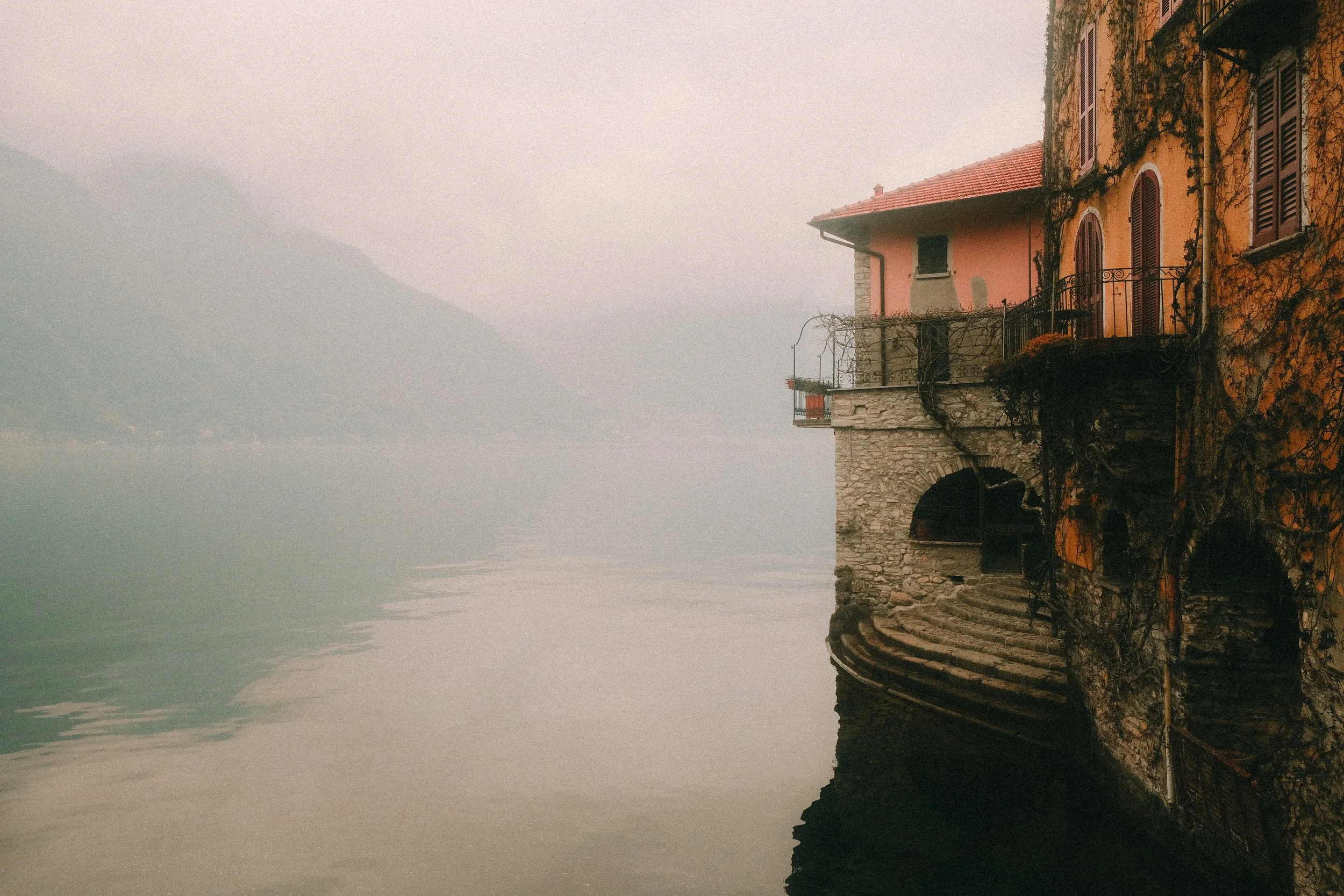 Cliffside houses overlooking a foggy lake with mountains in the background.