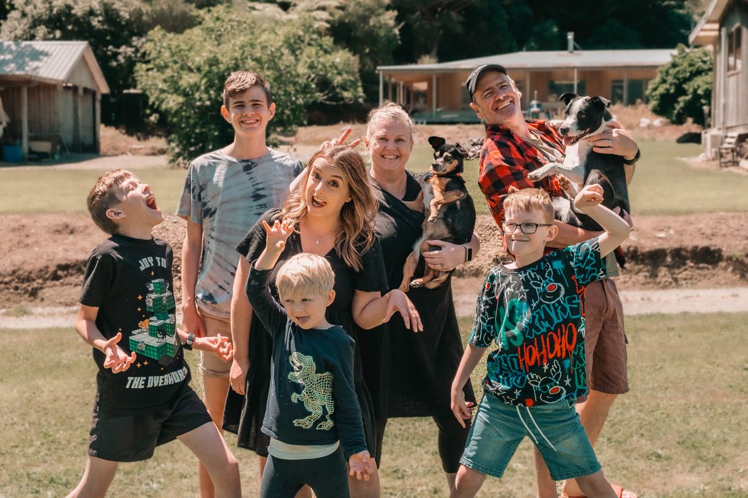 A family outdoor gathering with children and two adults holding small dogs, all smiling and having fun in a backyard with houses and trees in the background.
