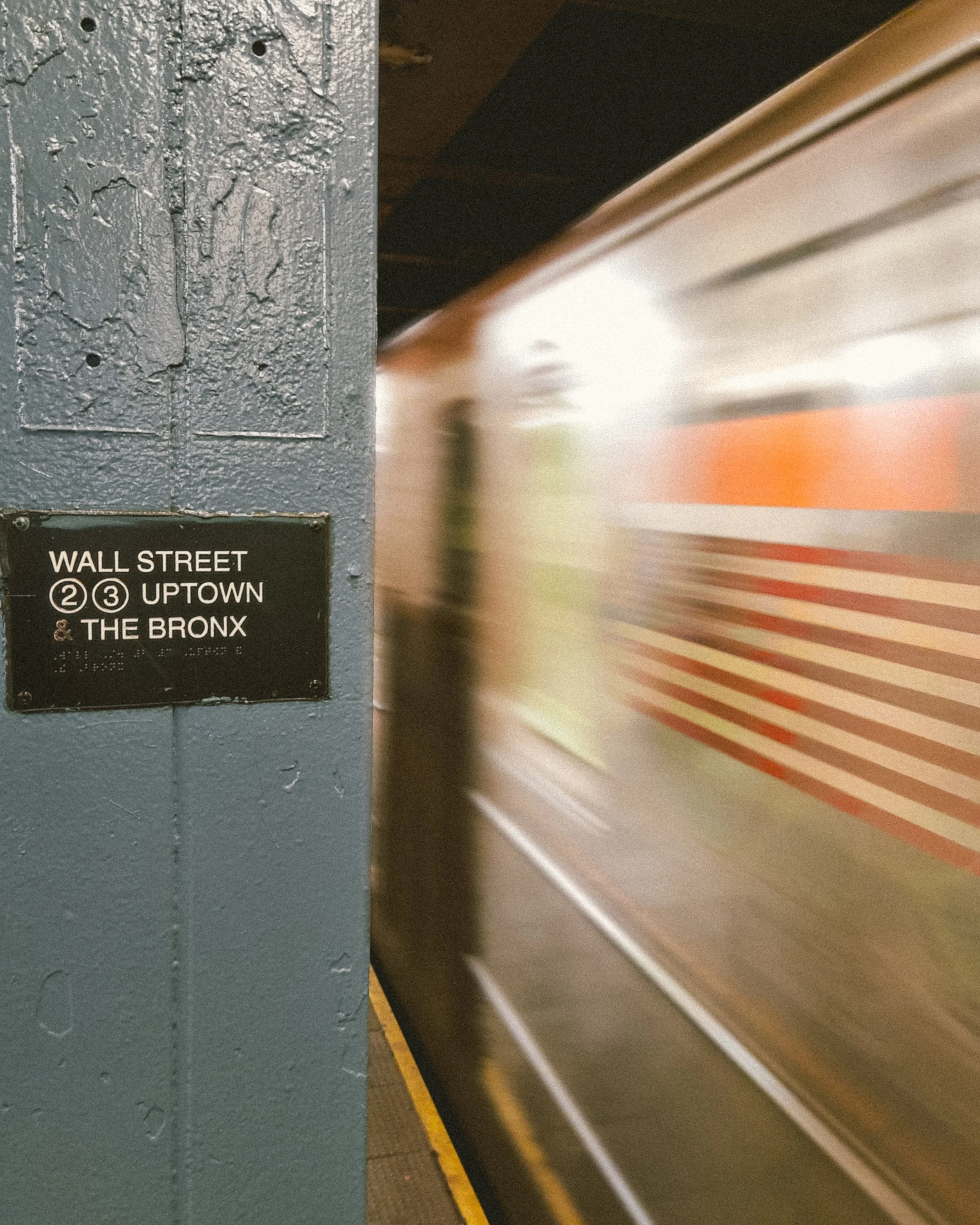 Subway train arriving at a station with a sign for Wall Street, Uptown, and The Bronx on the pillar.