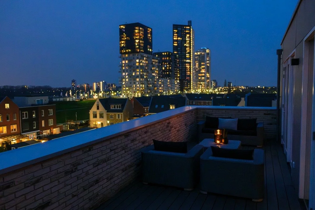 Nighttime city view from a rooftop terrace with outdoor seating and lit candles.