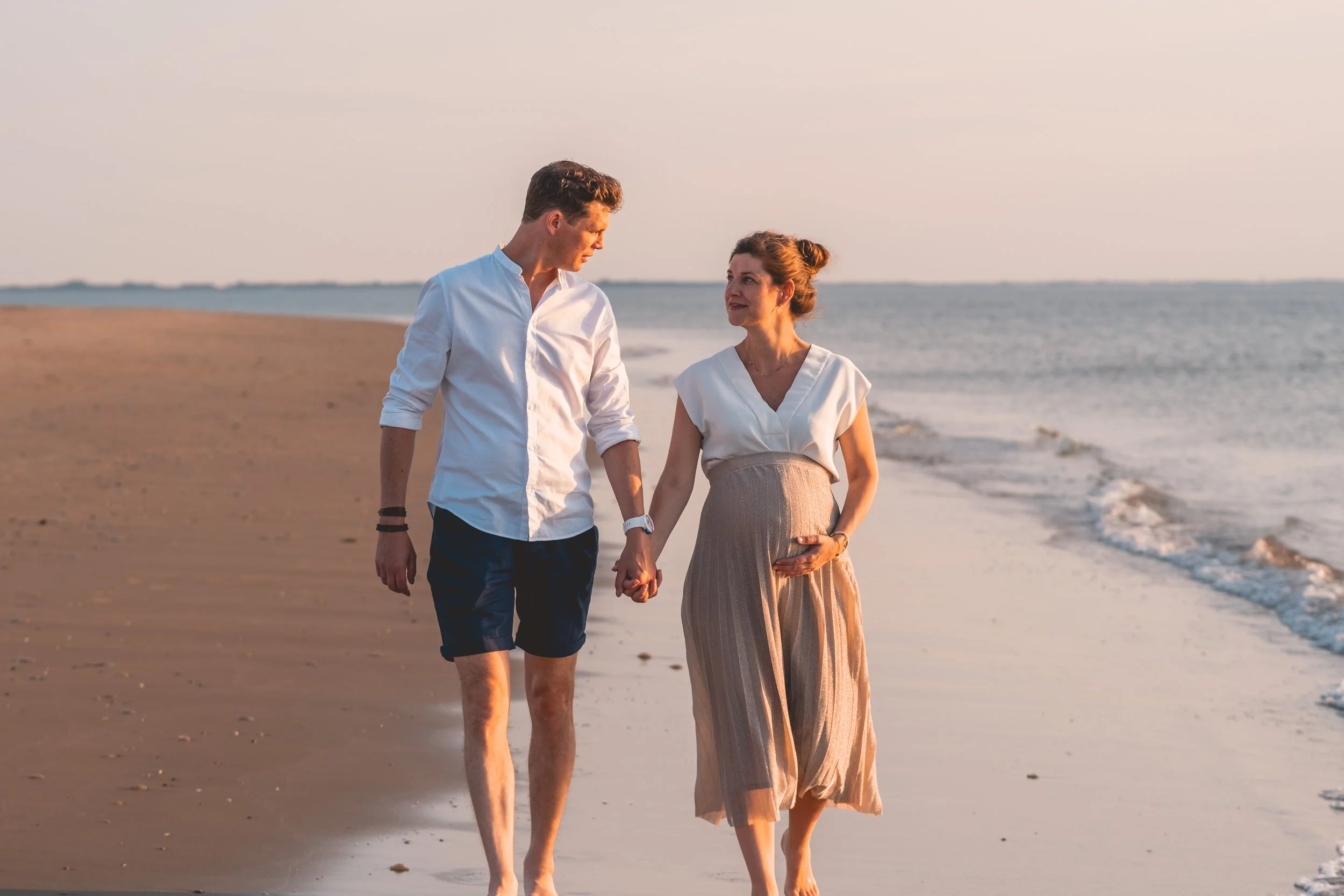 A man and woman walking hand-in-hand along the beach at sunset, with the ocean in the background.