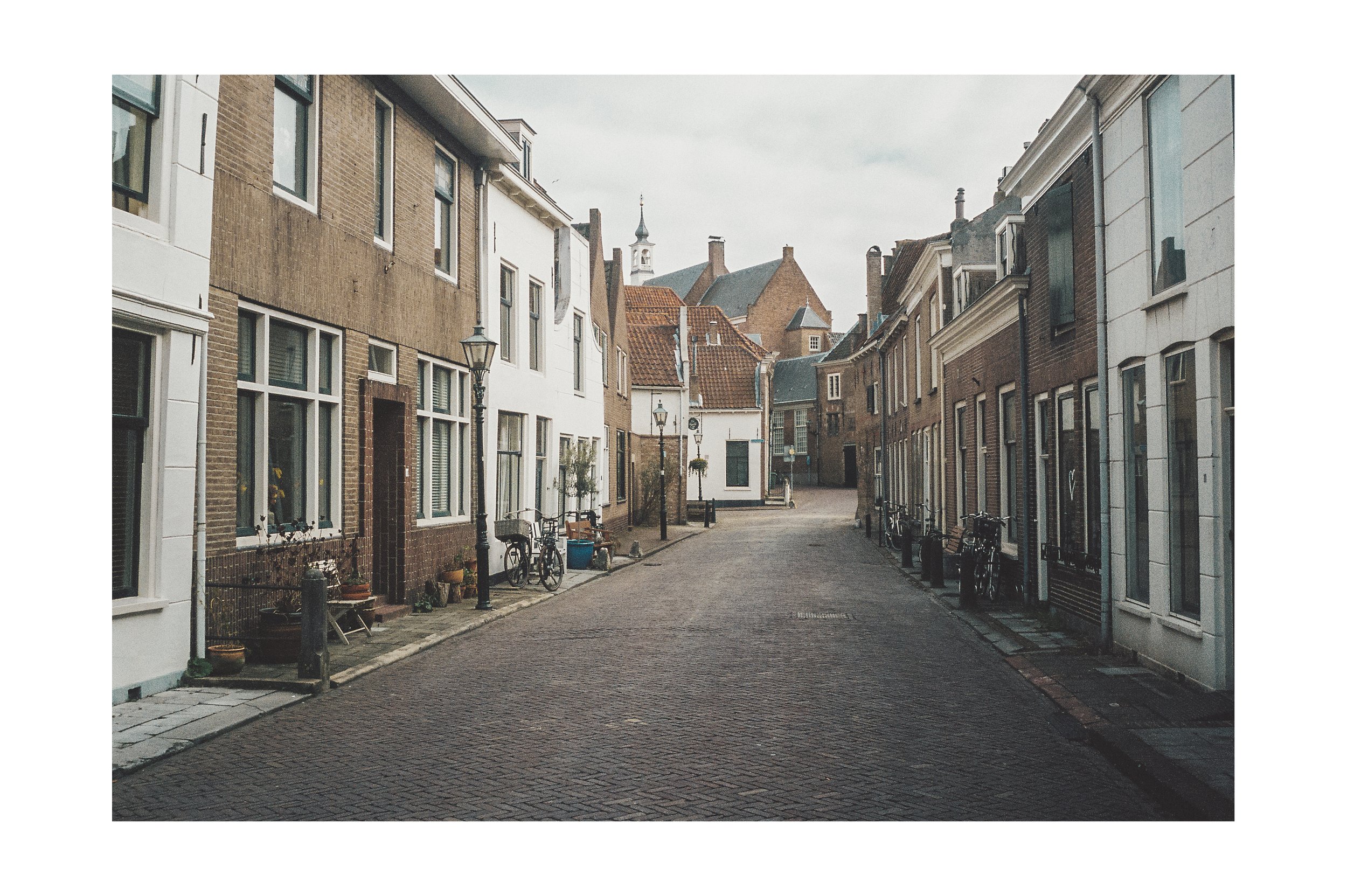 Quiet cobblestone street lined with colorful residential buildings and bicycles parked along the curb, under a cloudy sky.