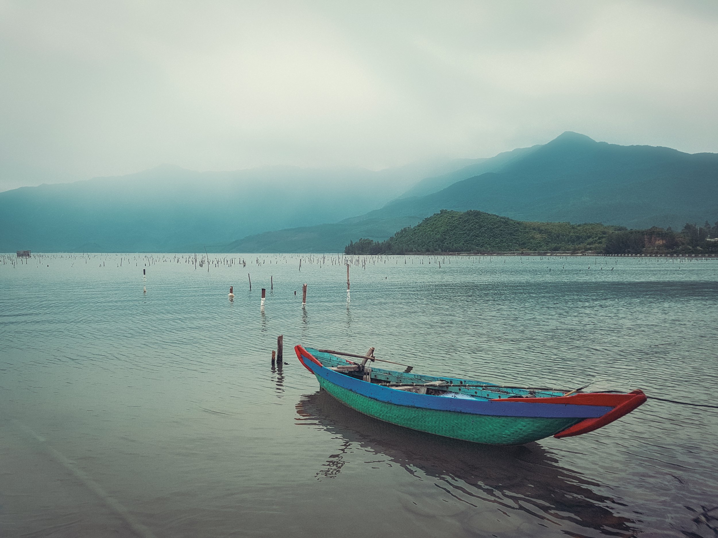 Colorful boat on calm lake with mountains and cloudy sky in background.