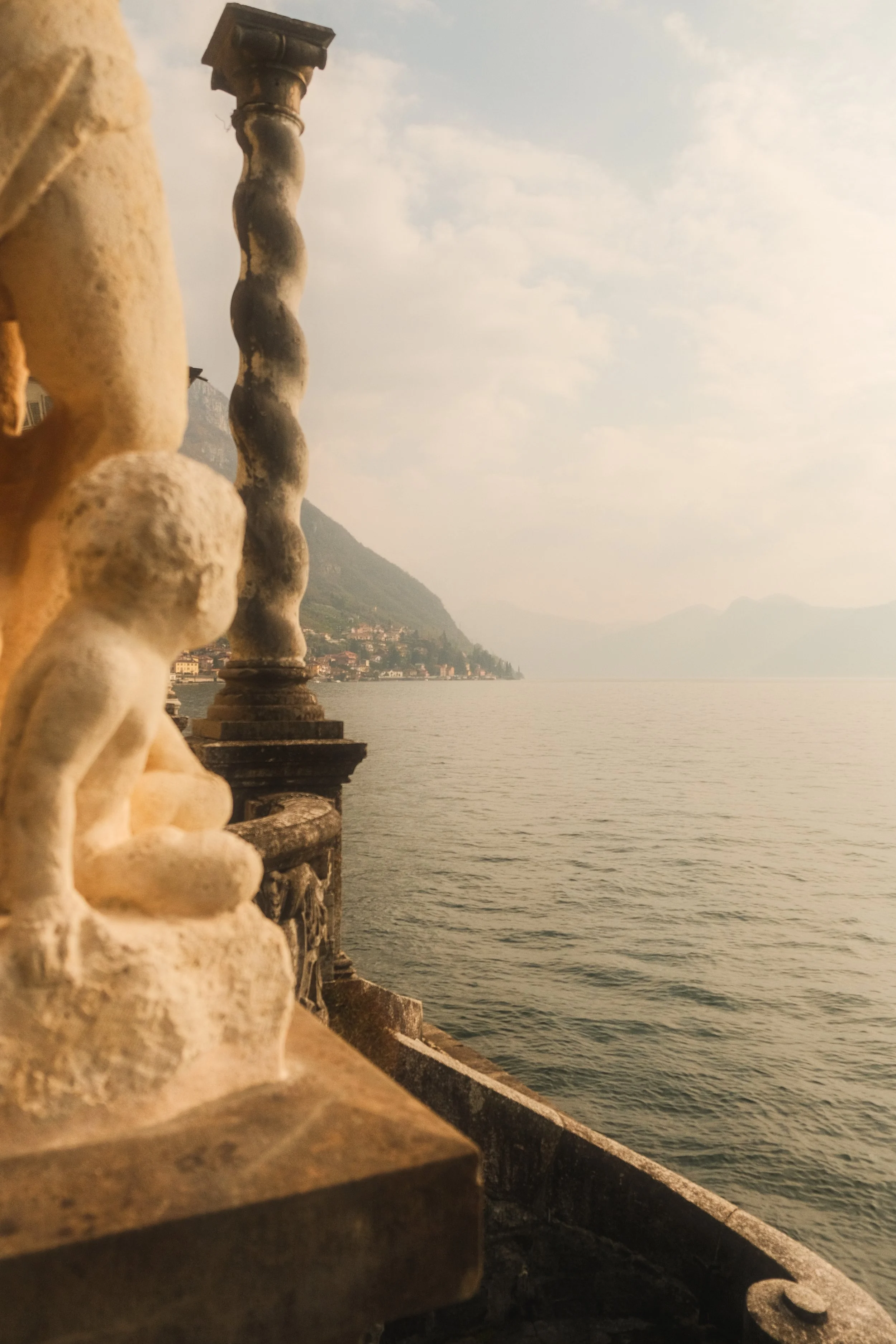 View of a lake with hills in the distance, seen from a stone balcony with an ornate balustrade.