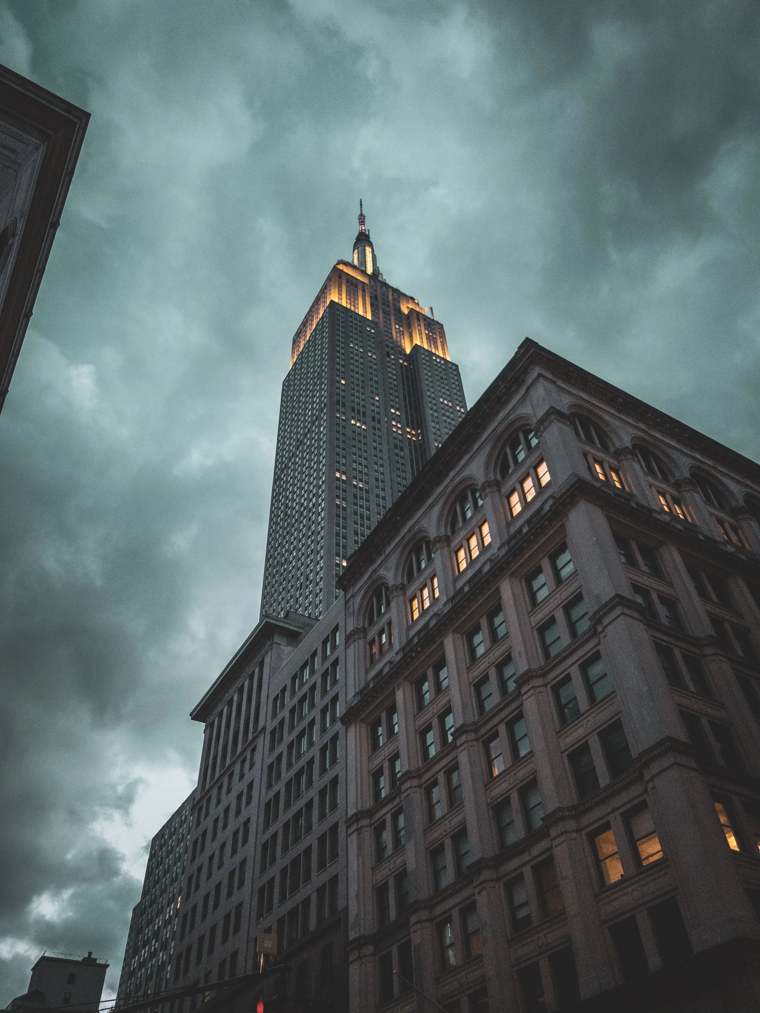 Tall skyscraper with lit windows, viewed from below with darker clouds in the sky.