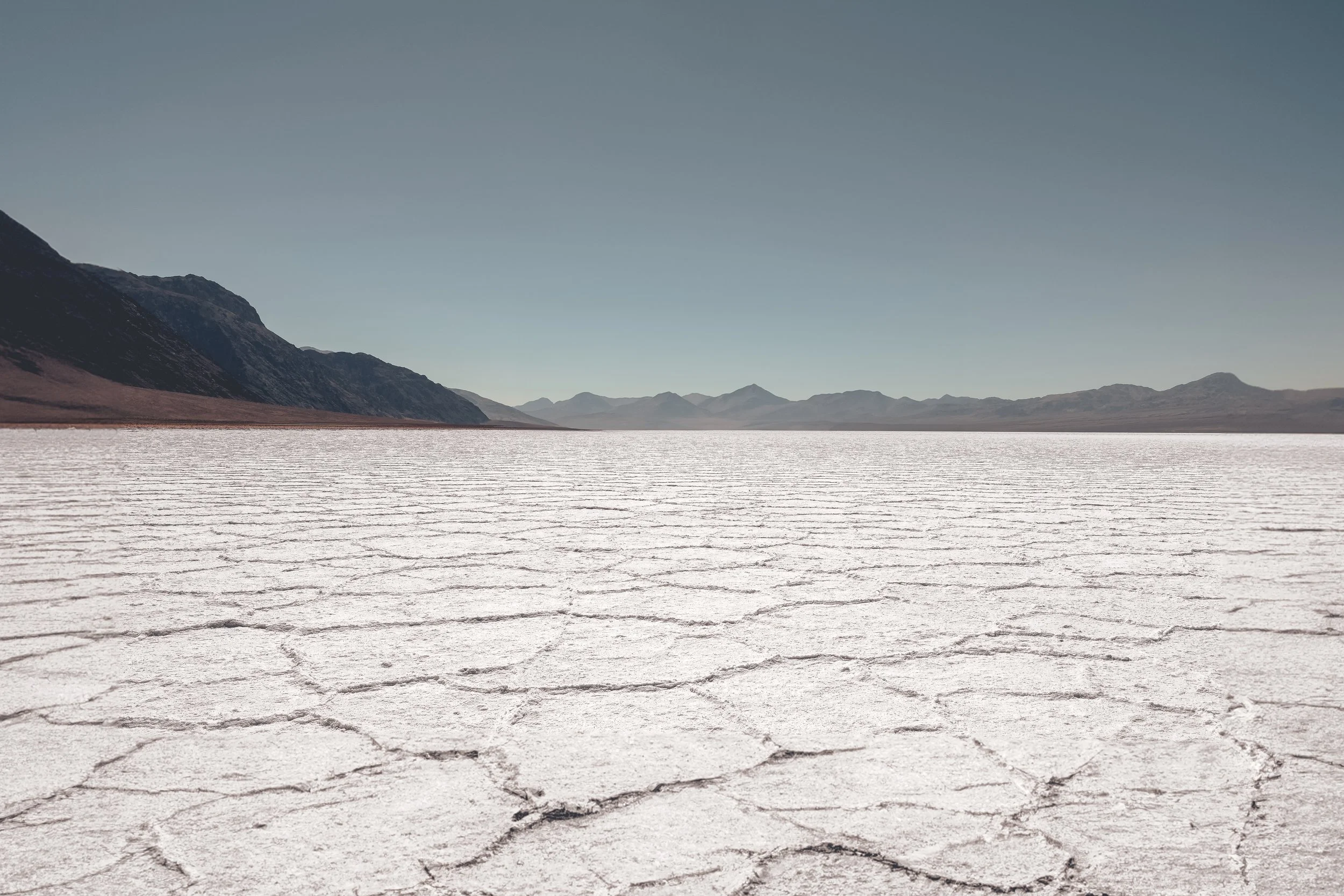 Dry, cracked salt flats with distant mountains under a clear blue sky.