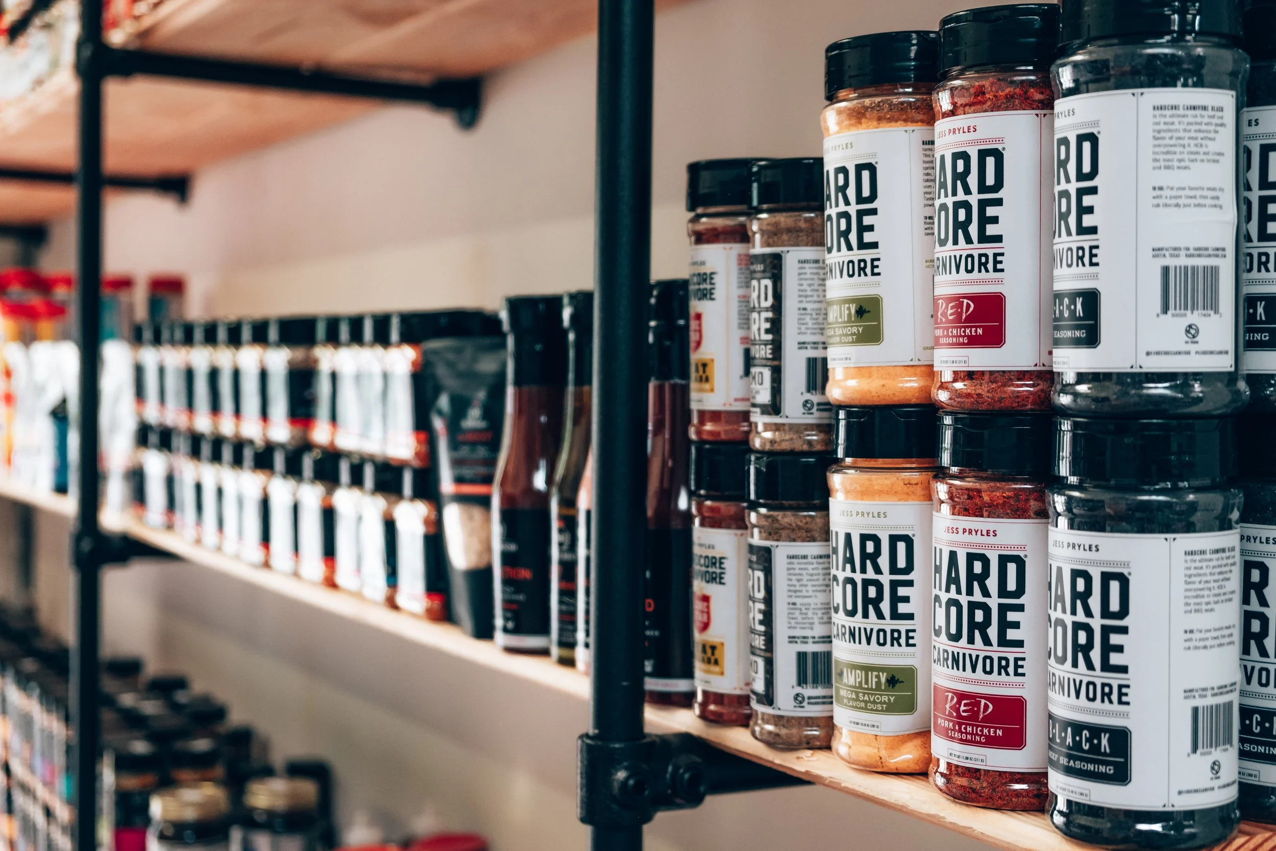 Shelves stocked with jars of savory seasoning blends from Hard Core Carnivore, including amplify, red, and black flavors, in a grocery store.